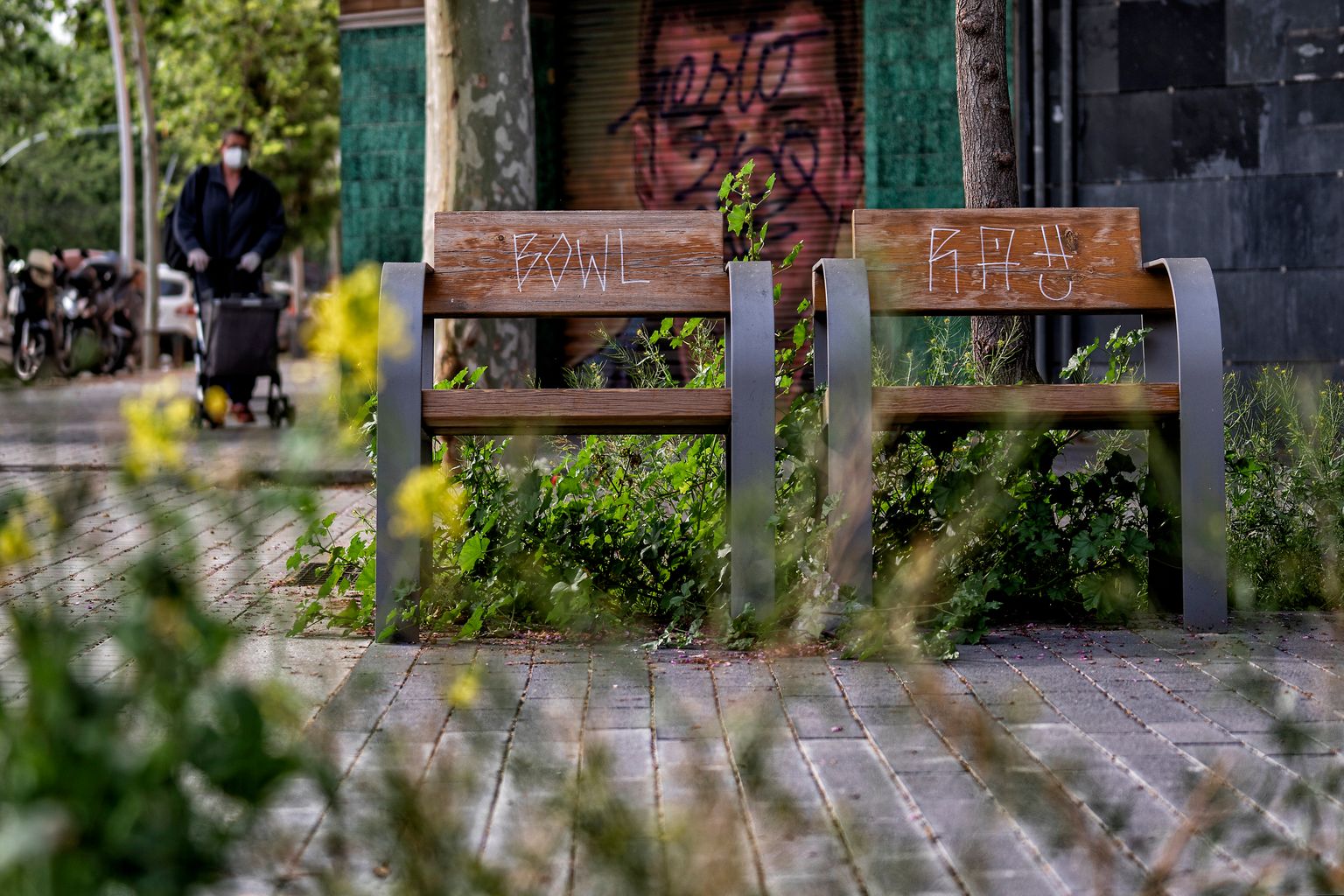 Bancos solitarios a los lados de la rambla del Poblenou y, al fondo, una persona con un carrito de la compra. Distrito de Sant Martí. Barrio del Poblenou. 