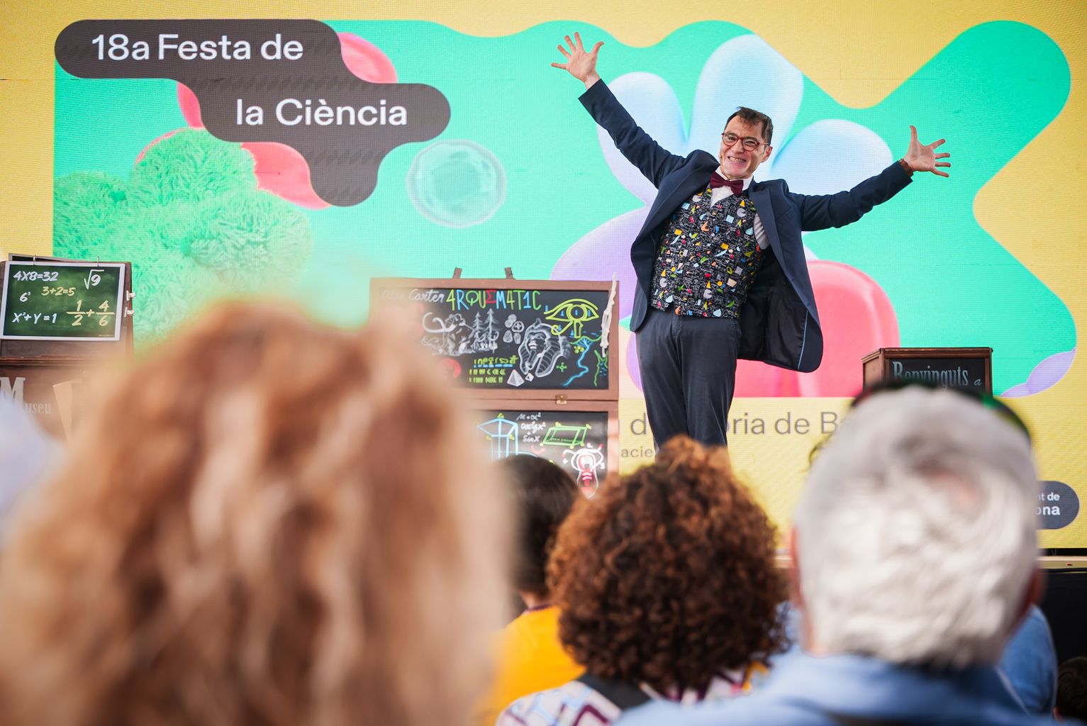 En primer plano, el presentador del espectáculo “Arquemàtic”, un show de matemáticas con mucha magia en el día de la Fiesta de la Ciencia, ante el público