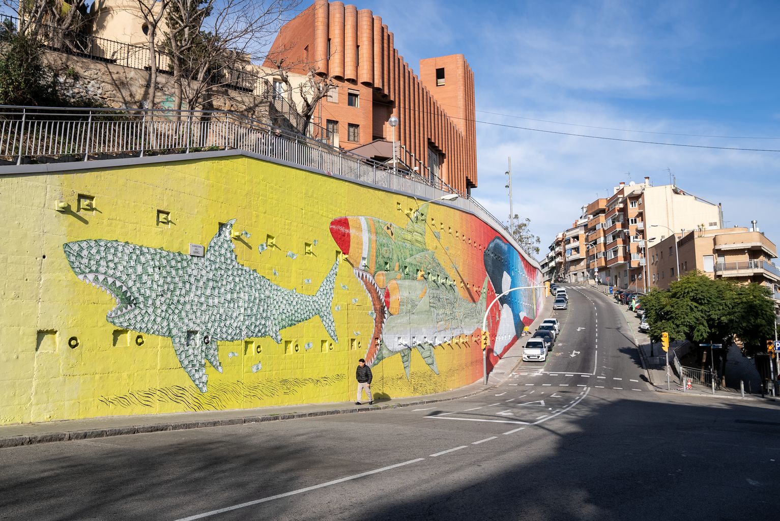 Nuevo mural del artista italiano BLU en el barrio del Carmel de Barcelona, que representa un tiburón hecho de billetes (capitalista) a punto de ser devorado por un tiburón con elementos bélicos, que al mismo tiempo está a punto de ser devorado por una orca que representa el cambio climático.