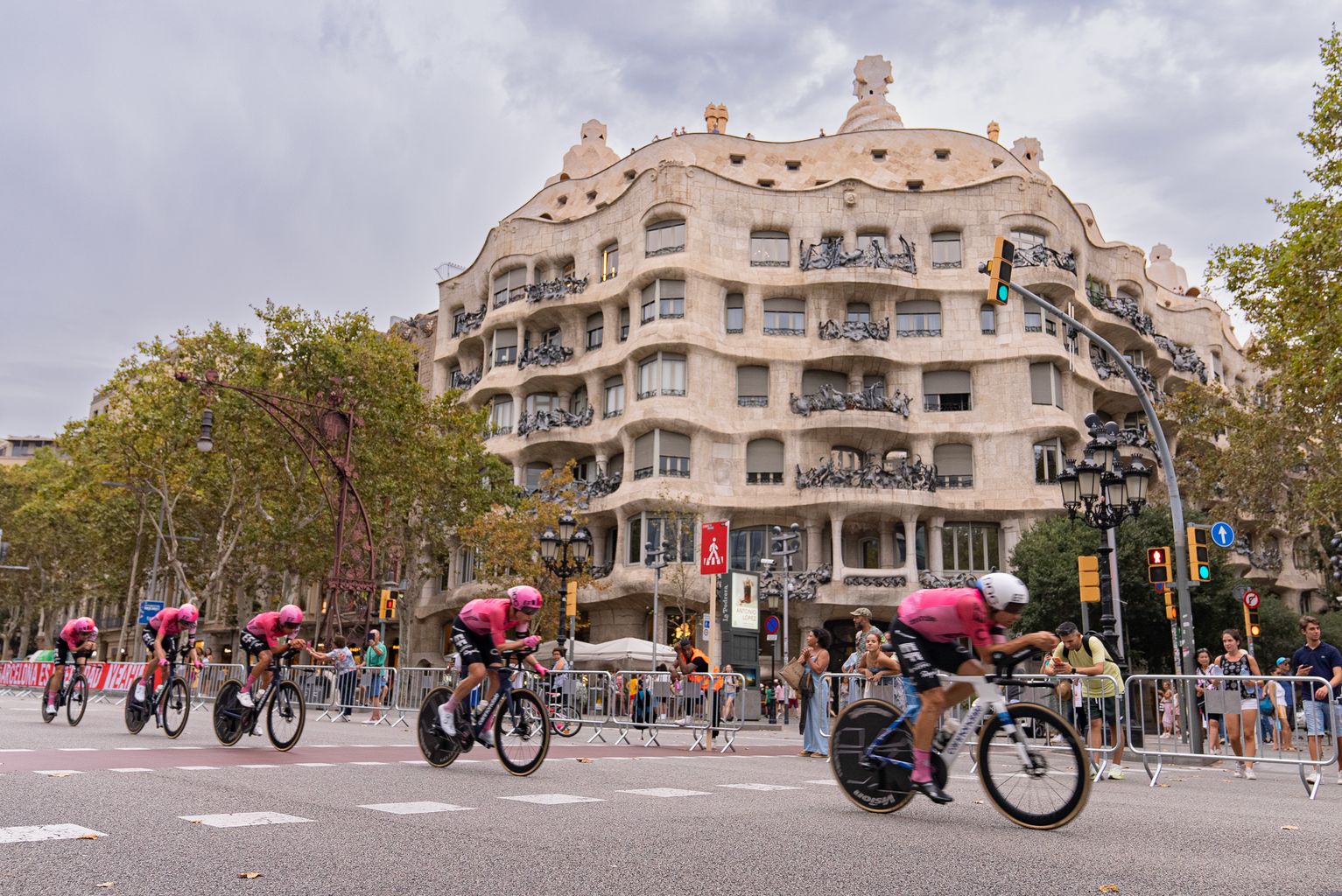 Ciclistas participantes en la competición 'La Vuelta a España' circulando por la zona habilitada en el paseo de Gràcia. A su lado, público animando. Al fondo, el edificio de La Pedrera del arquitecto Antoni Gaudí