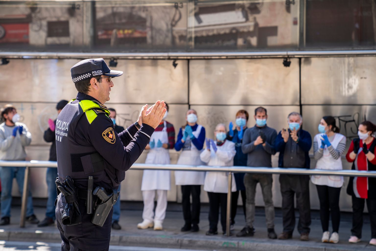 Agent de la Guàrdia Urbana aplaudint als paradistes del Mercat d'Hostafrancs que se'ls miren des de la vorera
