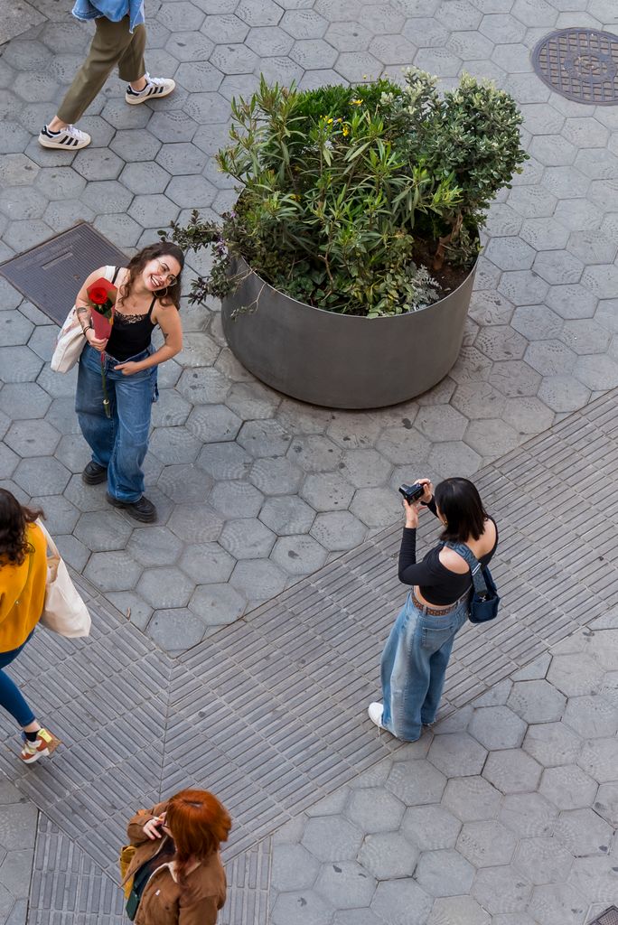 Vista des de dalt d'una noia jove fent una fotografia a una altra noia que té una rosa a la mà el dia de Sant Jordi