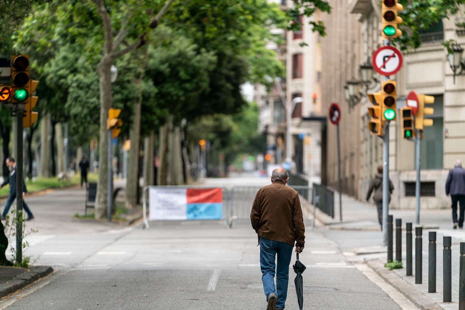 Home amb un paraigua a la mà caminant per les zones ampliades per a vianants de la xarxa d'itineraris segurs al lateral de l'avinguda Diagonal