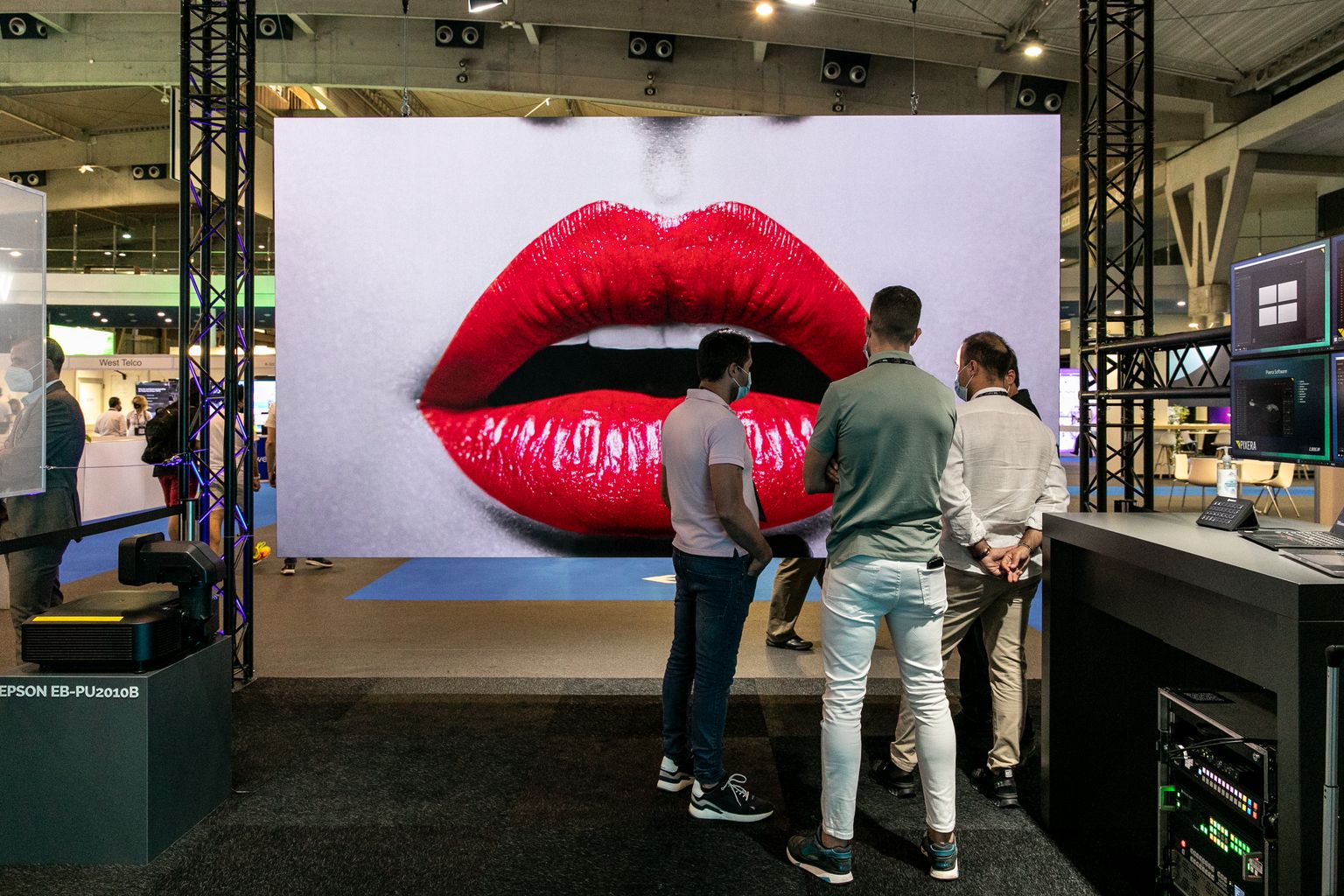Estands del Saló Integrated Systems Europe (ISE) dedicats al món de la indústria audiovisual amb els assistents al voltant d’una gran pantalla amb uns llavis pintats de vermell