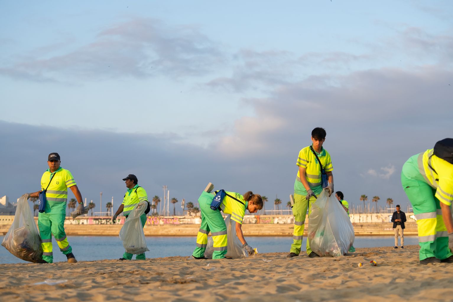 Operarios de limpieza recogiendo los residuos de la playa de la Nova Icària después de la verbena de San Juan.