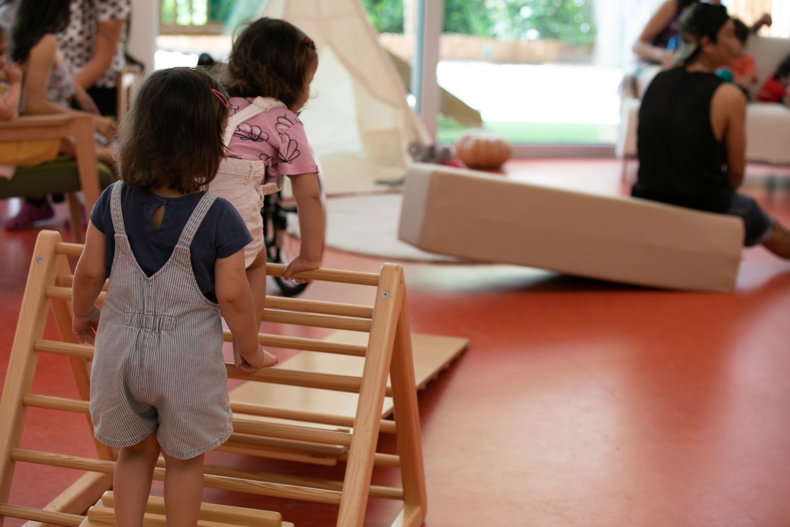 Unas niñas trepan por unas escaleras de madera en la sala de juegos del Espacio Familiar de Crianza Municipal Els Gats (EBM Els Gats).