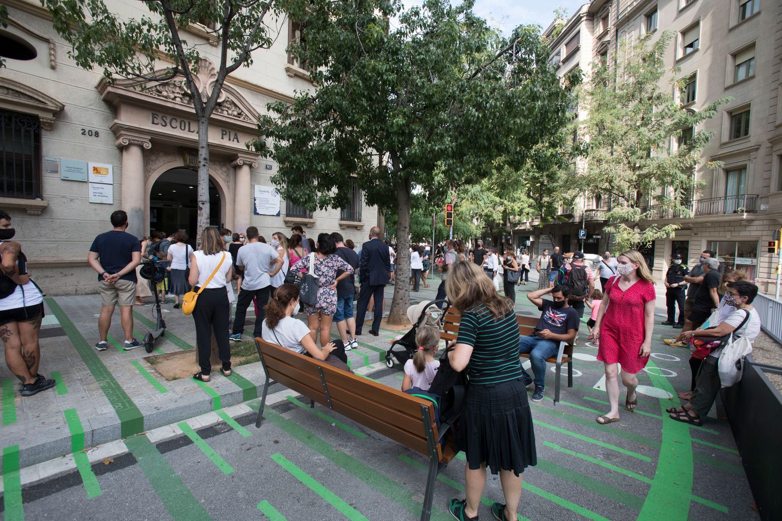 Famílies esperant els nens a la sortida de classe a la zona pacificada davant de l’Escola Pia Balmes, alguns d’ells estan asseguts als bancs