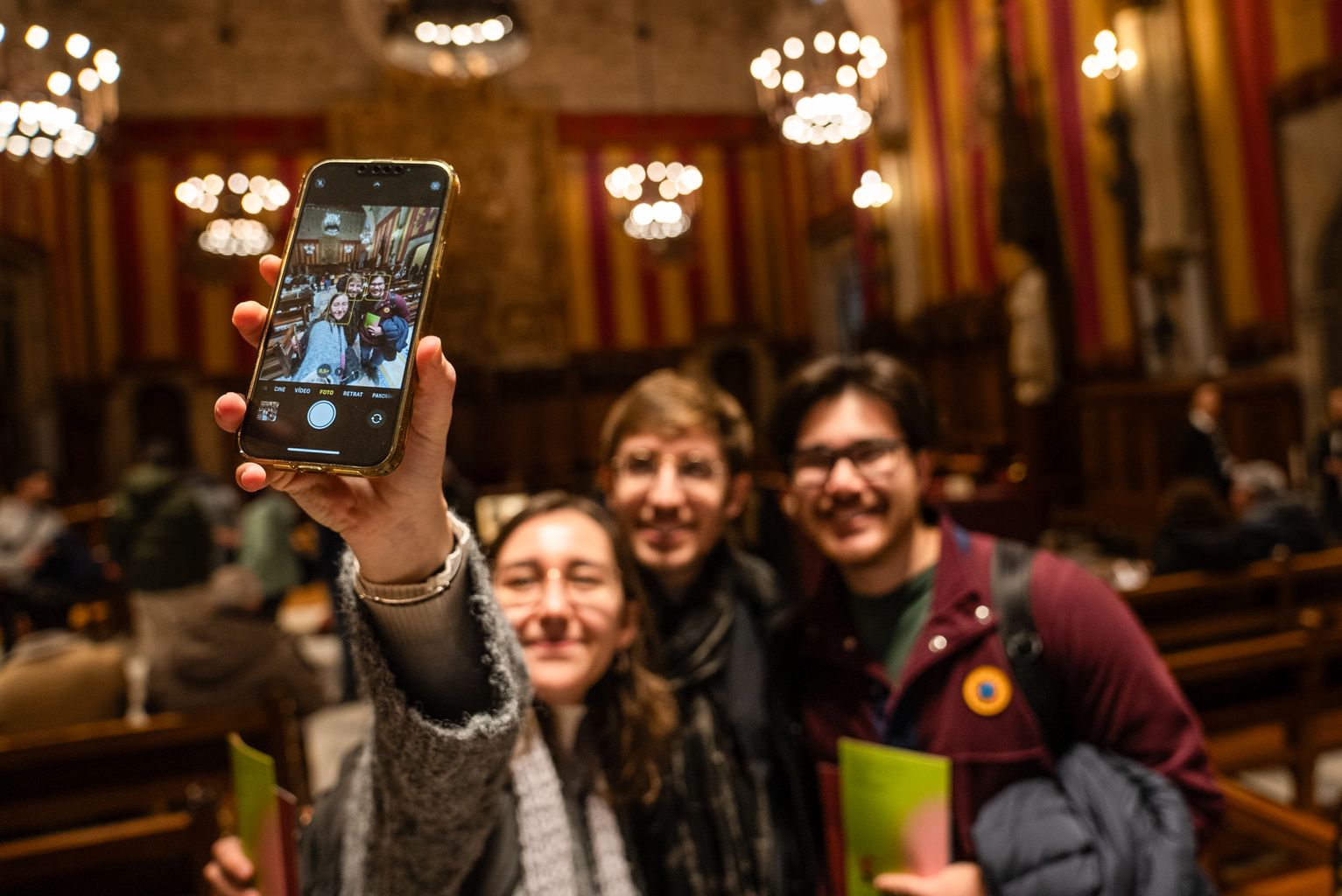 Tres joves es fotografien amb el mòbil al Saló de Cent a les jornades de portes obertes de l'Ajuntament