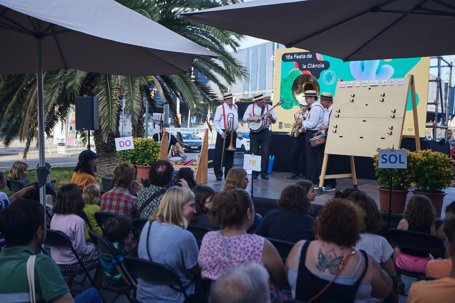 Un grup musical toca diferents instruments dalt de l'escenari durant la presentació de "Els secrets de la música" de la 16a Festa de la Ciència a la Rambla de Prim.