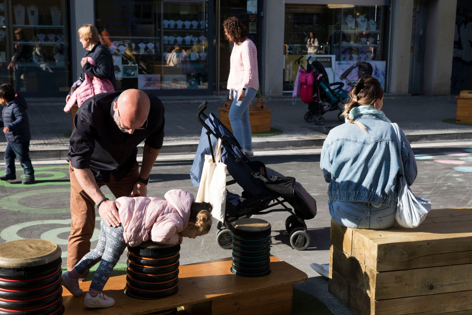 Un pare juga amb la filla amb un joc de fusta a l'entorn pacificat del “Protegim les escoles” de l'Escola Barcelona i l'EBM Can Novell.
