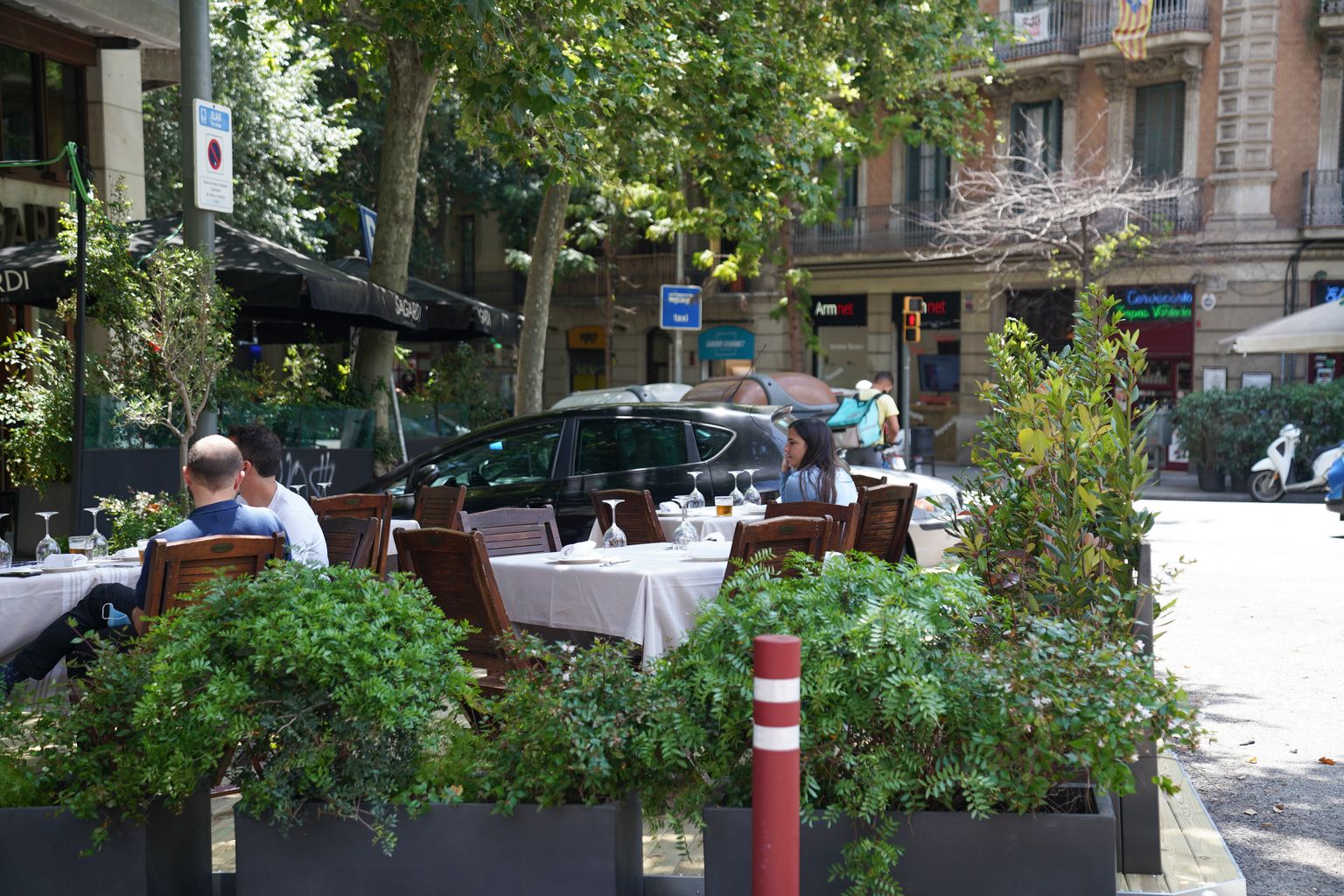 Clients prenent una beguda abans de dinar en un dels nous prototips de terrassa en xamfrà d’un restaurant. Al voltant, les jardineres i una pilona els separen de la zona pels vehicles
