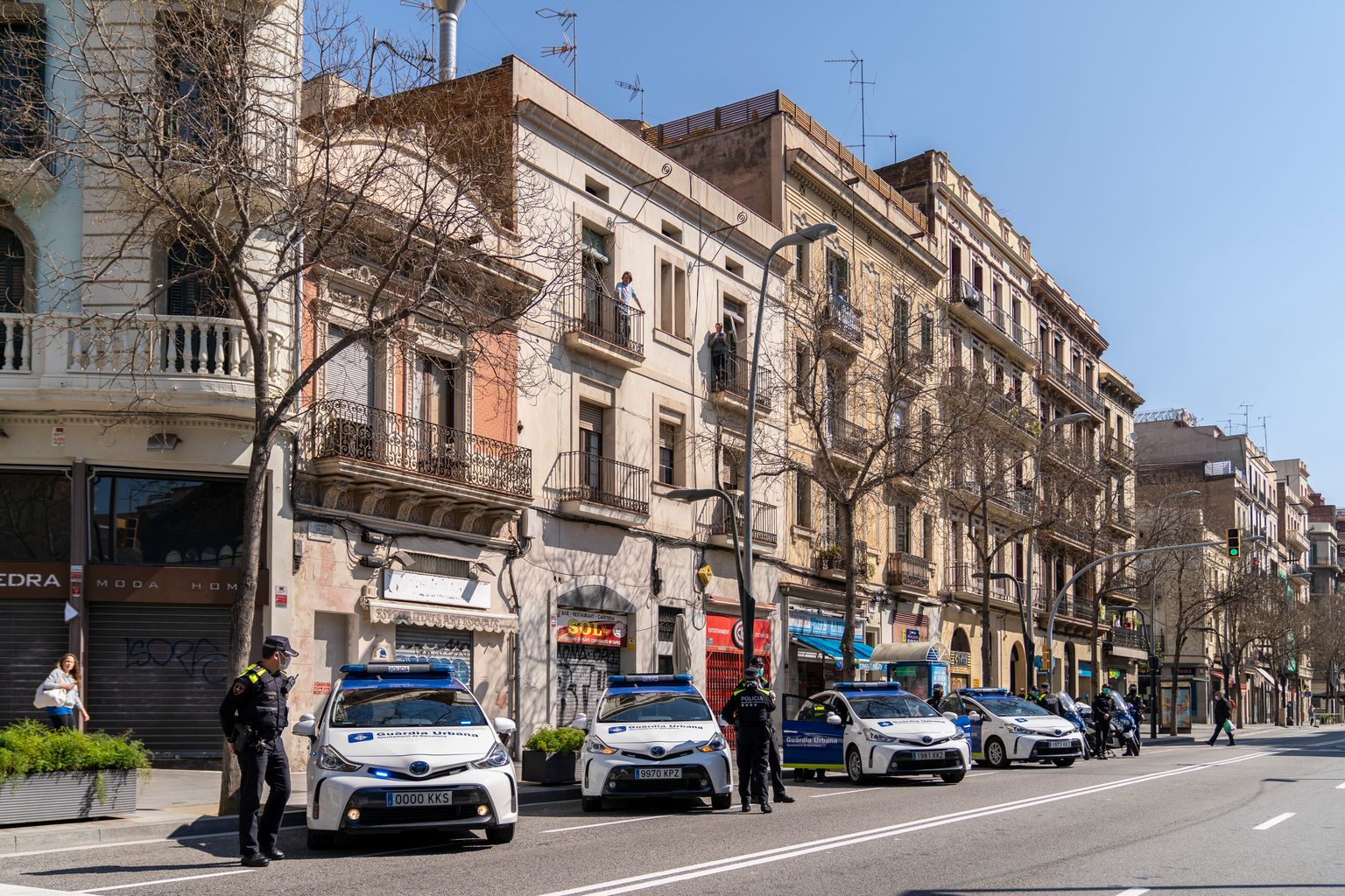 Cotxes i agents de la Guàrdia Urbana amb mascaretes i guants parats davant del Mercat d'Hostafrancs per retre l'homenatge als treballadors dels Mercats Municipals