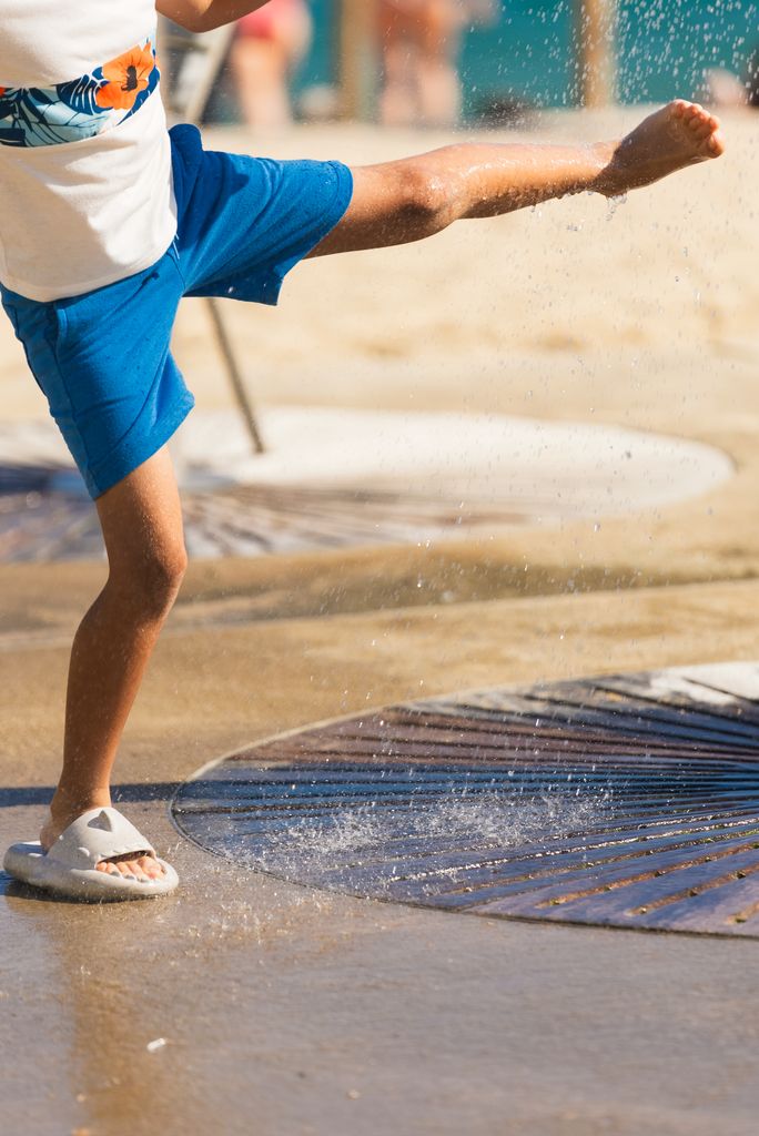 Un niño se moja un pie en la ducha de la playa