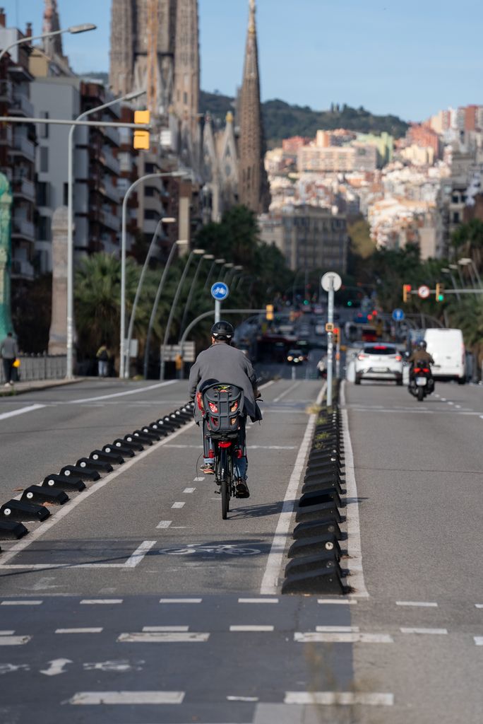 Ciclista pedala amb una cadireta i un infant al darrere en direcció a la Sagrada Família