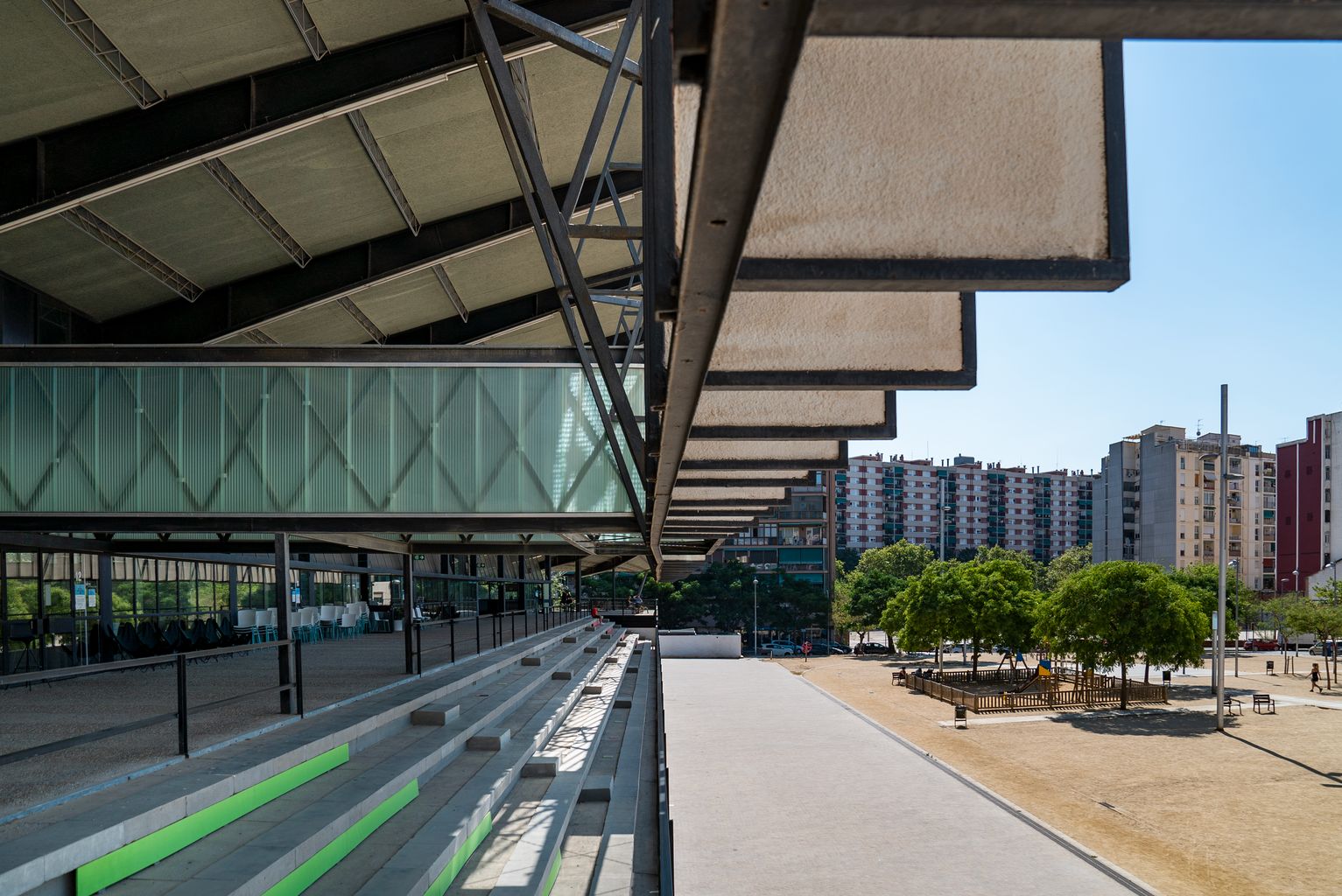 Graderies d’accés a l’edifici del Canòdrom - Parc de Recerca Creativa, amb una coberta en voladís que la protegeix del sol i on la gent seu