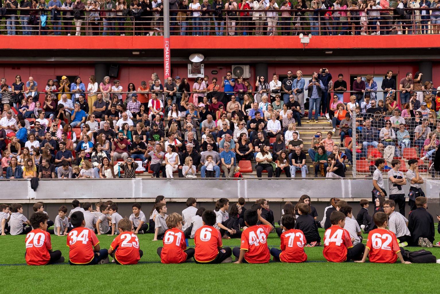 Ambient a les graderies i infants, membres d’equips del Club Esportiu Martinenc, durant l’acte d’inauguració de la nova gespa i presentació dels equips del club.