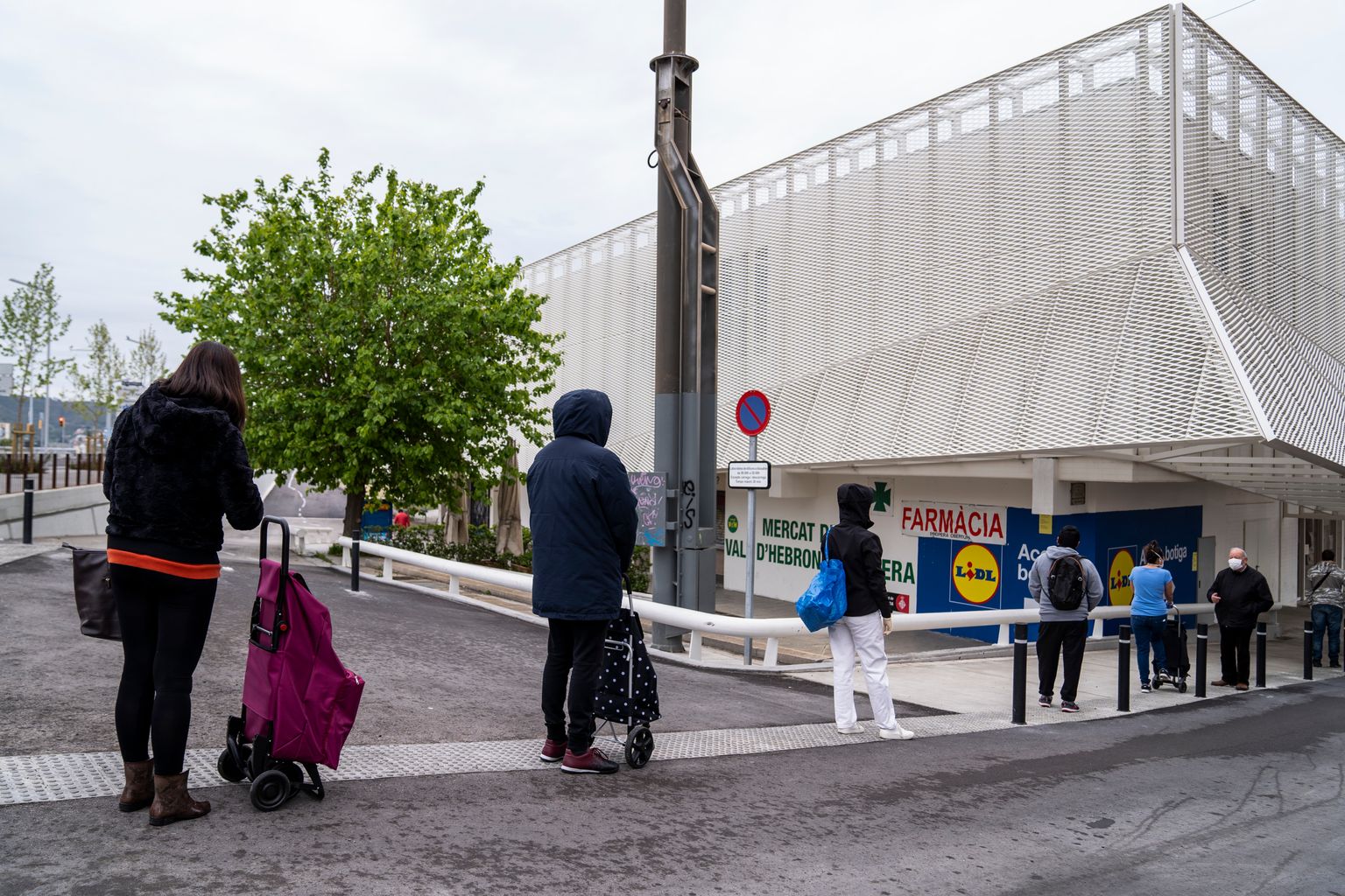 Cua de gent als voltants del Mercat de la Vall d’Hebron on hi ha també un hipermercat esperant per entrar. Molts d’ells porten mascaretes i guarden la distància de seguretat