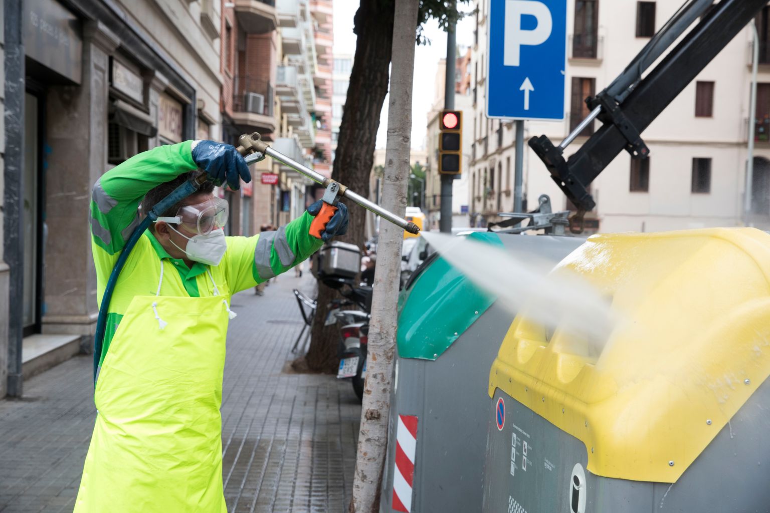 Un treballador del Servei de Neteja renta amb aigua a pressió uns contenidors situats a la plaça de Gal·la Placídia i els entorns