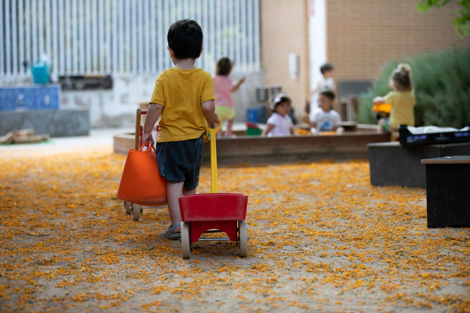 Un infant arrossega un carretó vermell pel pati de l'Escola Bressol Municipal Tres Turons