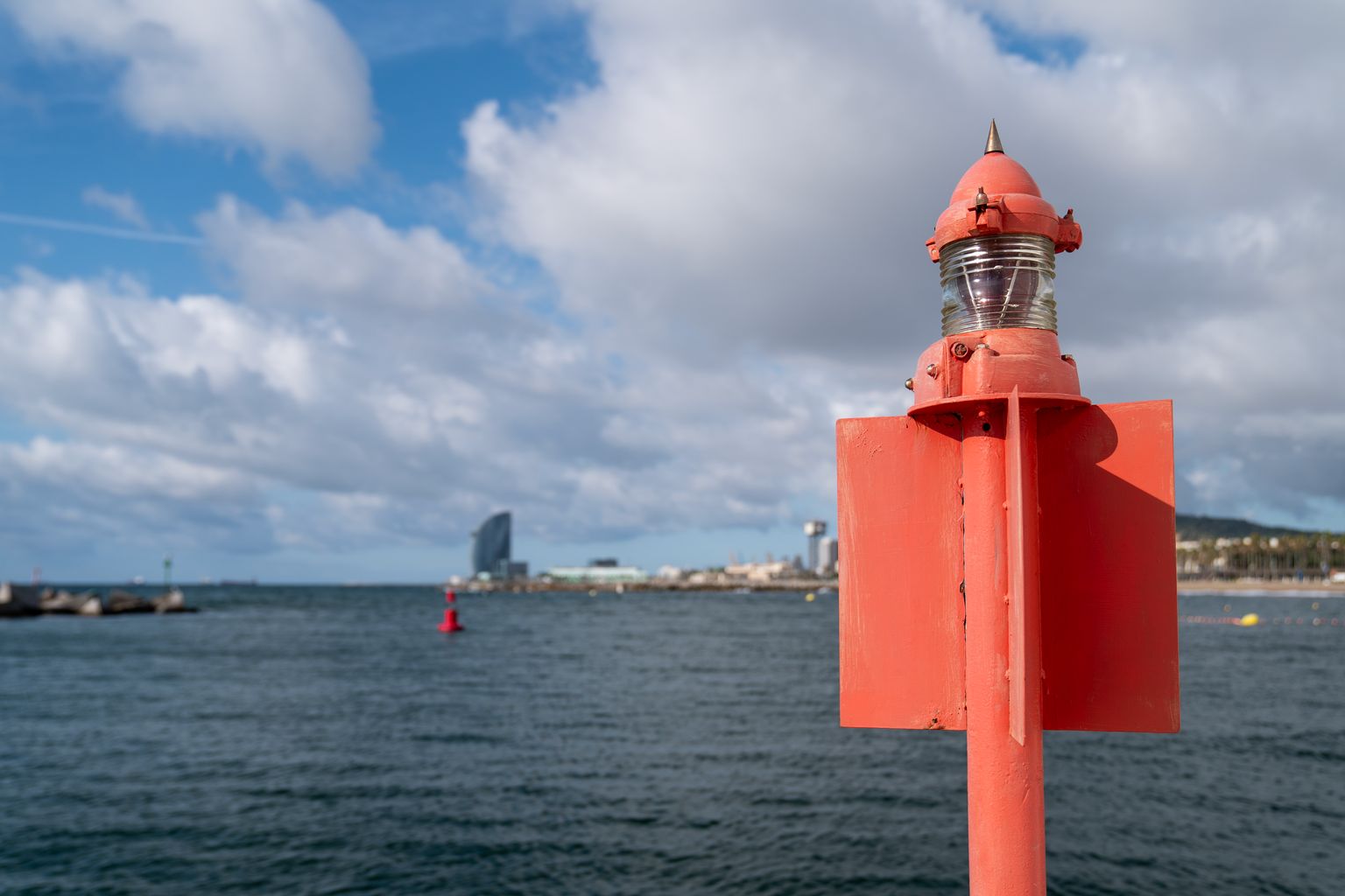 Pal vermell amb llum de referència al costat de l’estació Life iBathwater i boia vermella flotant al mar a l’altura de la platja del Somorrostro