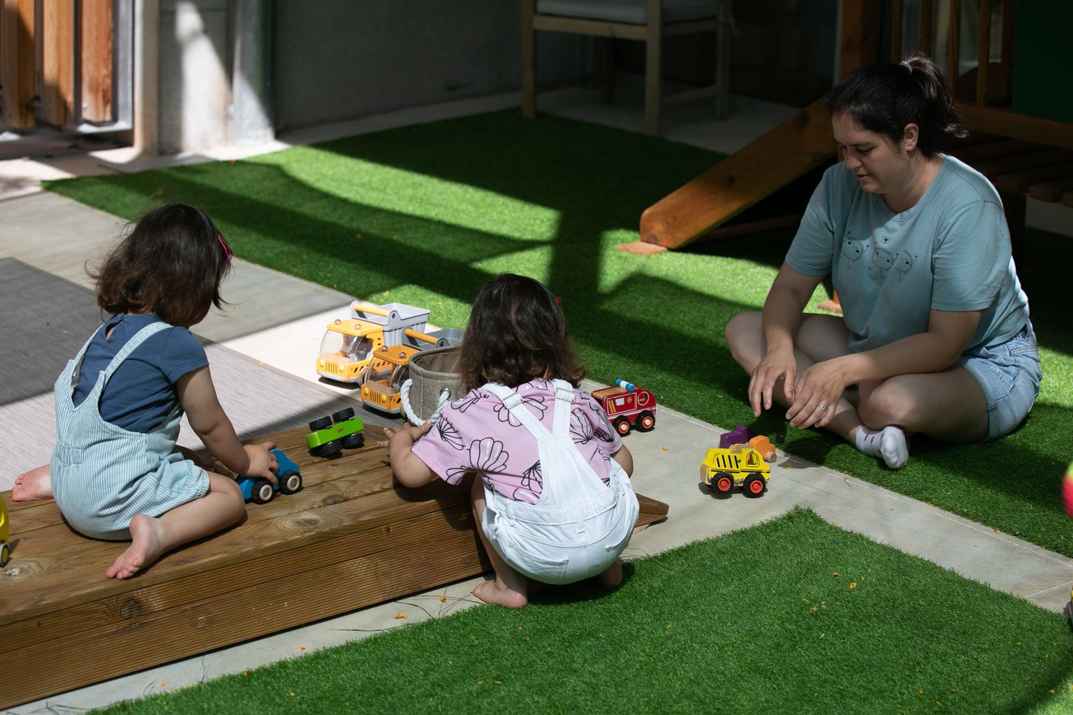 Una madre juega con dos niños en la zona exterior del Espacio Familiar de Crianza Municipal Els Gats (EBM Els Gats).