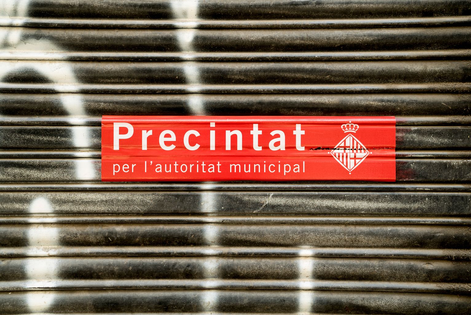 Persiana d'un local amb l'adhesiu de precinte municipal