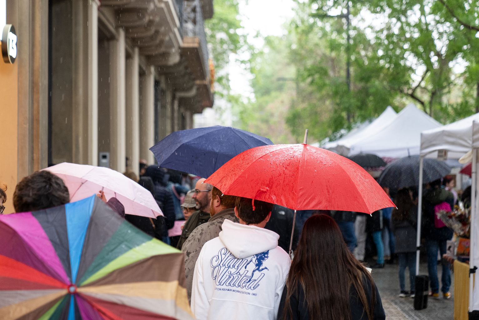 Gente con paraguas visitando los puestos de Sant Jordi del paseo de Sant Joan