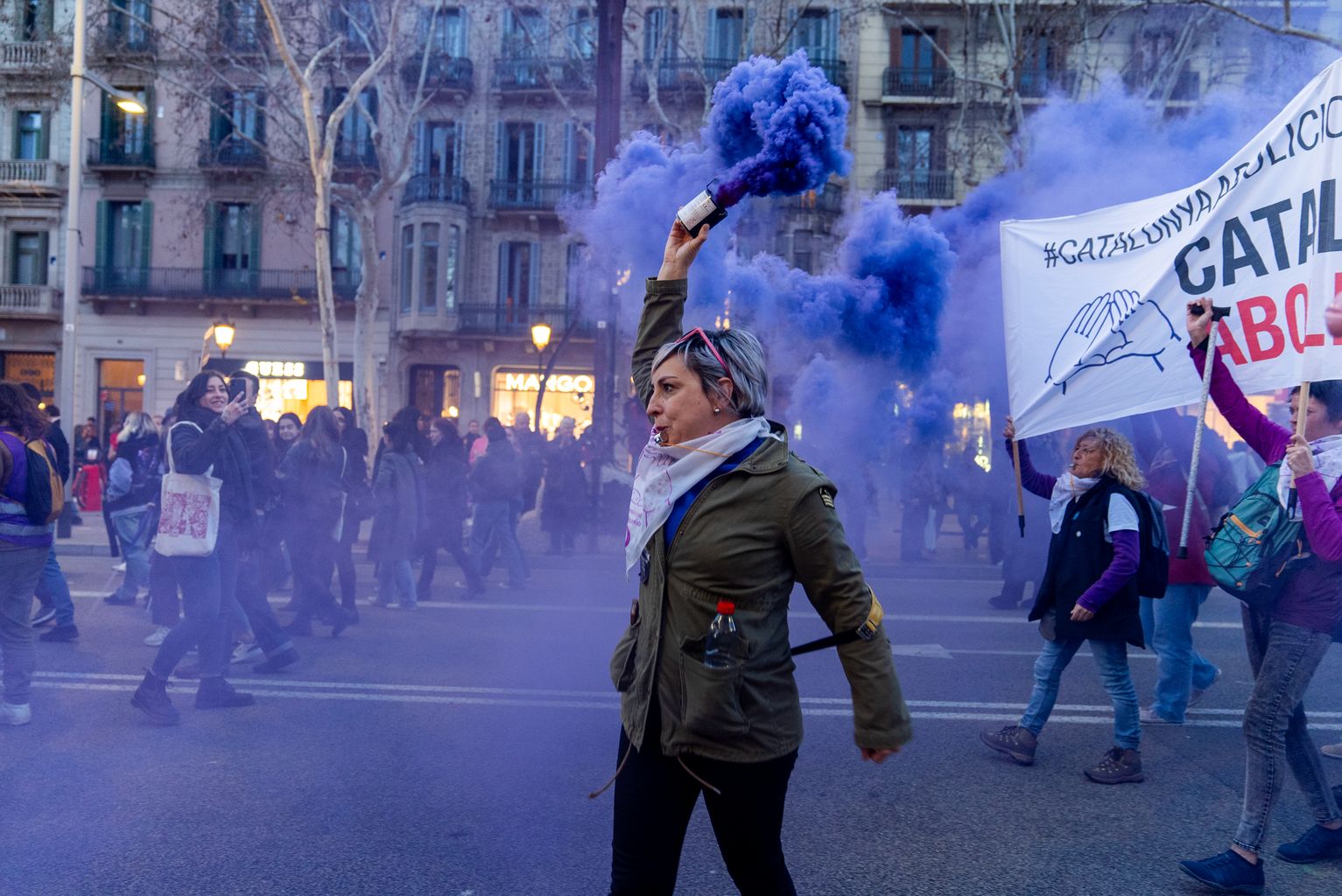 Una mujer con una bomba de humo de color lila durante la marcha de la manifestación del Día Internacional de las Mujeres en el paseo de Gràcia de Barcelona.