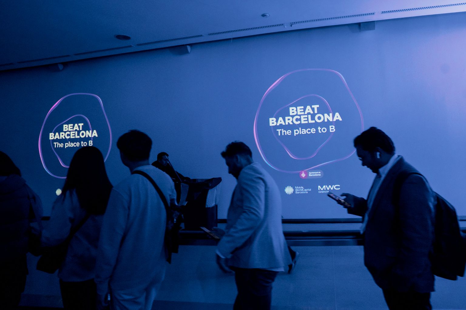 Congressistes caminant per l'interior del recinte firal que acull el Mobile World Congress 2024. Darrere, un anunci del Beat Barcelona