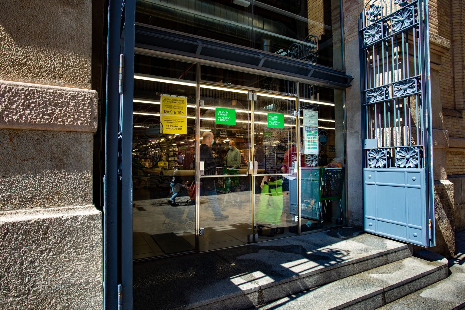 Entrada al Mercat de Sants on es veu gent a punt de sortir-ne amb les compres. Districte de Sants. Barri de Sants. 