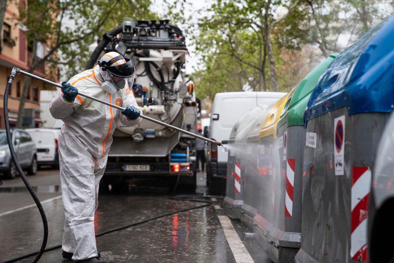 Un operario de una empresa de servicios de limpieza opera una lanza de agua a presión para desinfectar los contenedores