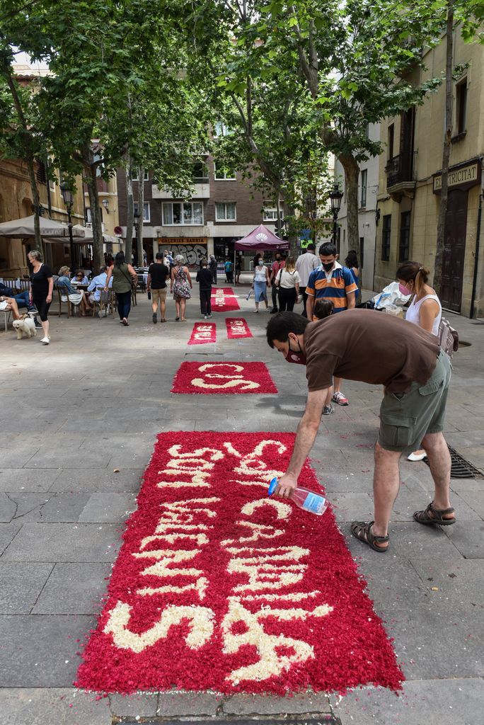 Un joven rocía con agua las flores de la alfombra floral de la ‘colla’ de los Castellers de Sarrià en la plaza del Consell de la Vila, donde se lee el lema “Som canalla, som valents”