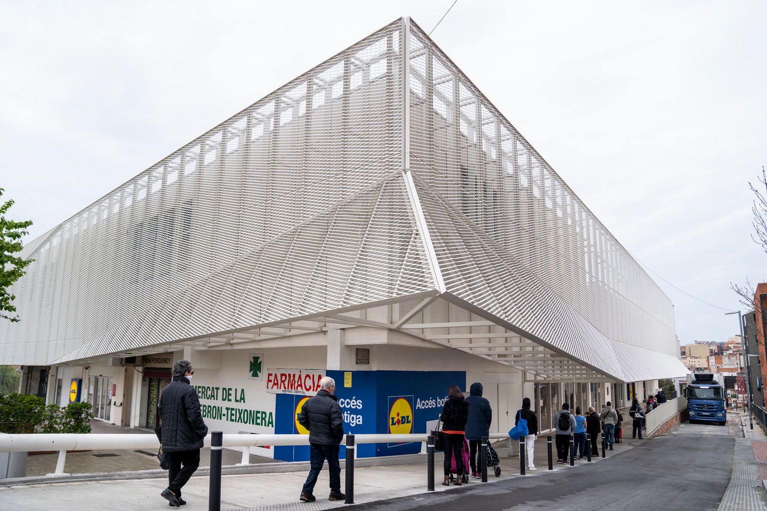 Cola de gente en los alrededores del Mercado de la Vall d’Hebron, donde hay también un hipermercado, esperando para entrar. Muchos de ellos llevan mascarillas y guardan la distancia de seguridad