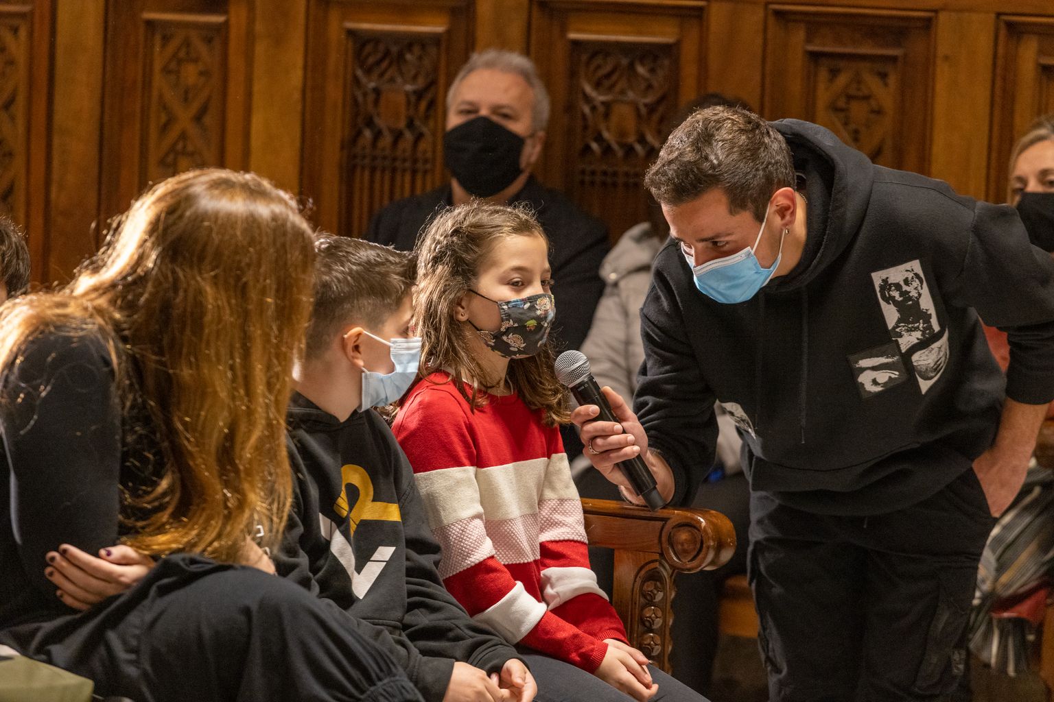 Una nena recita el seu fragment del Pregó dels Infants de les Festes de Santa Eulàlia al Saló de Cent mentre un home sosté el micròfon.