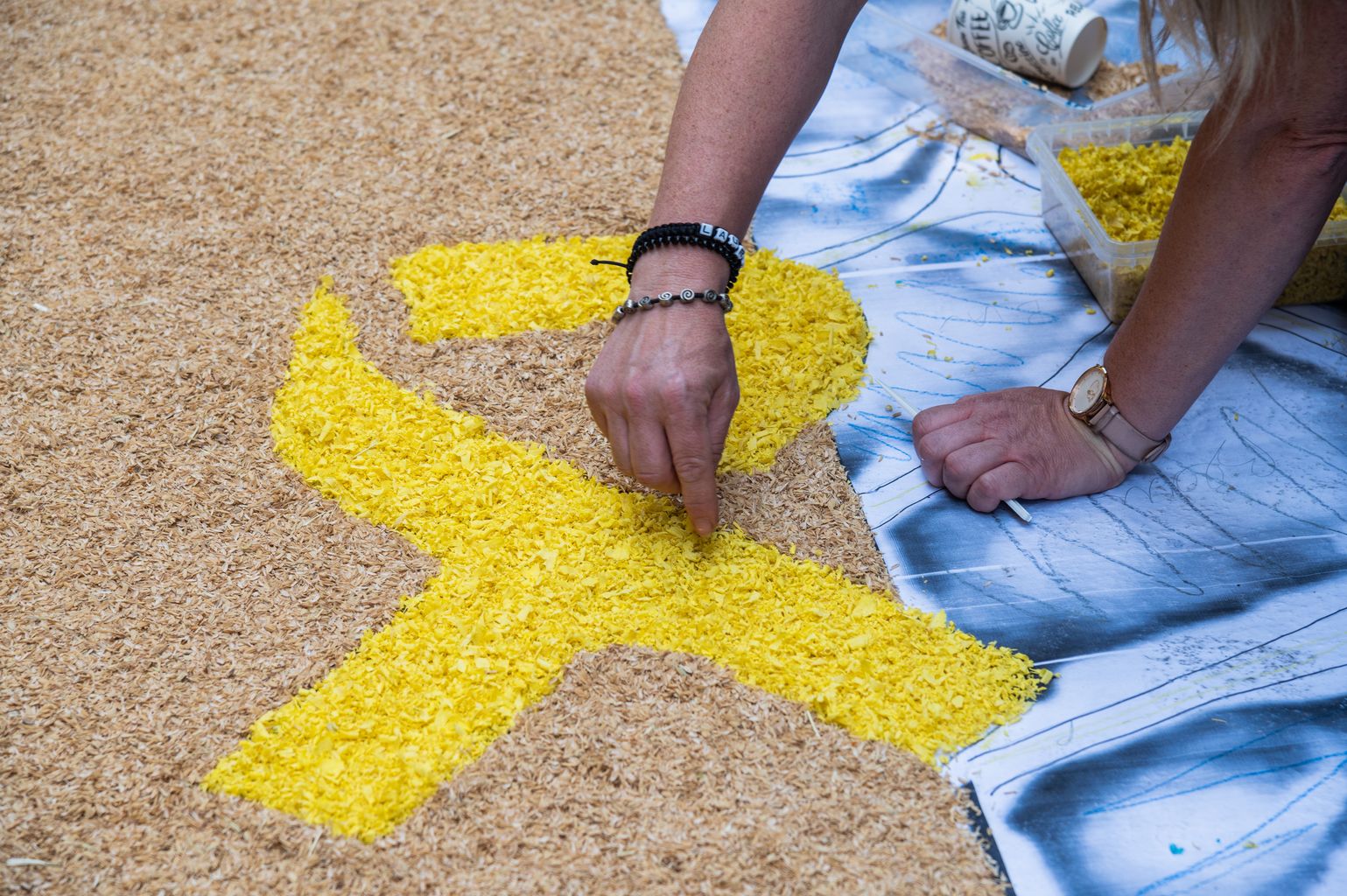 Una mujer rellena de serraduras de color amarillo un lazo en apoyo a los presos políticos que forma parte de la alfombra floral de la calle de la Llibertat, elaborada con motivo de la fiesta del Corpus