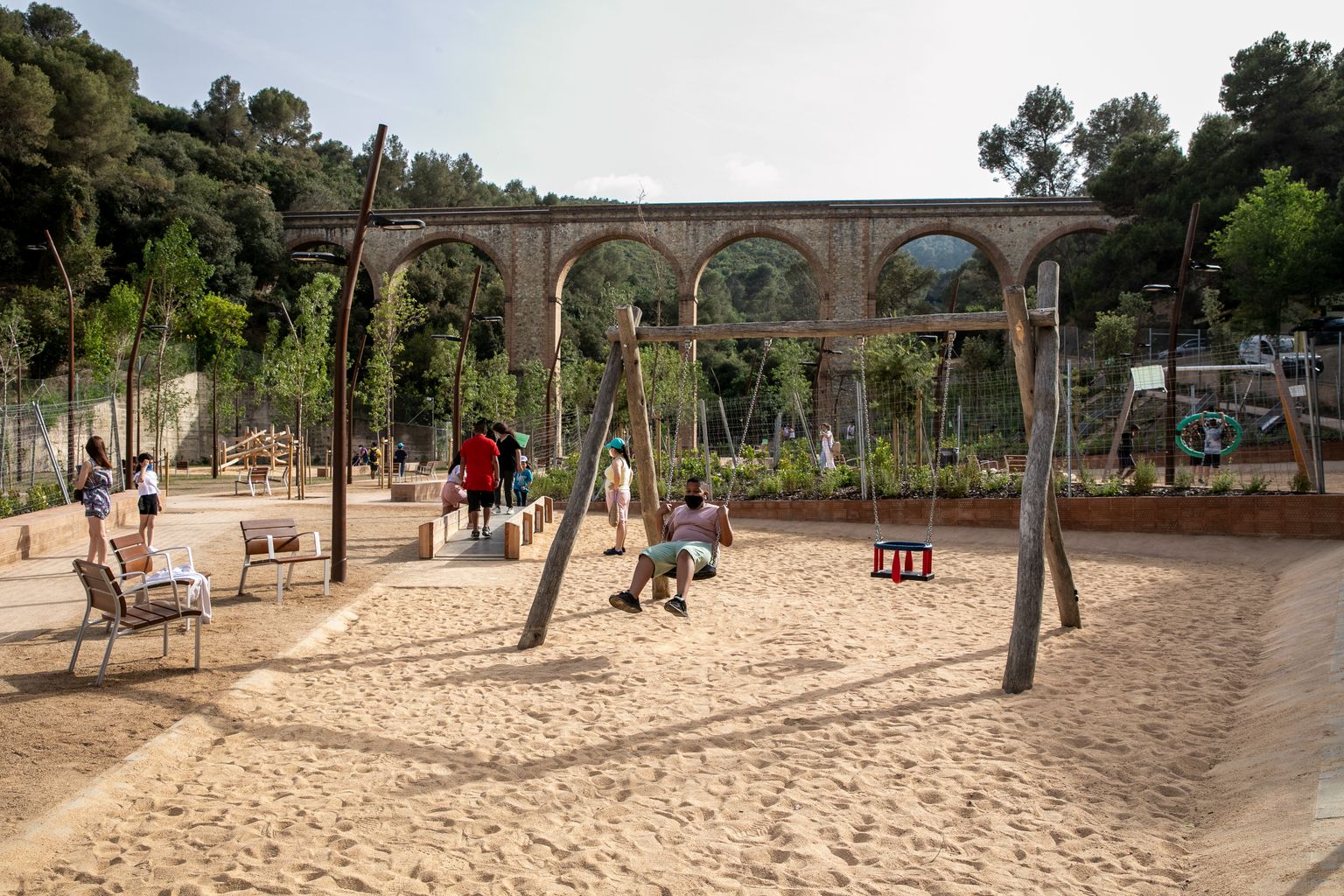 Àrea de joc infantil amb gronxadors del parc de l’Aqüeducte amb uns nens jugant