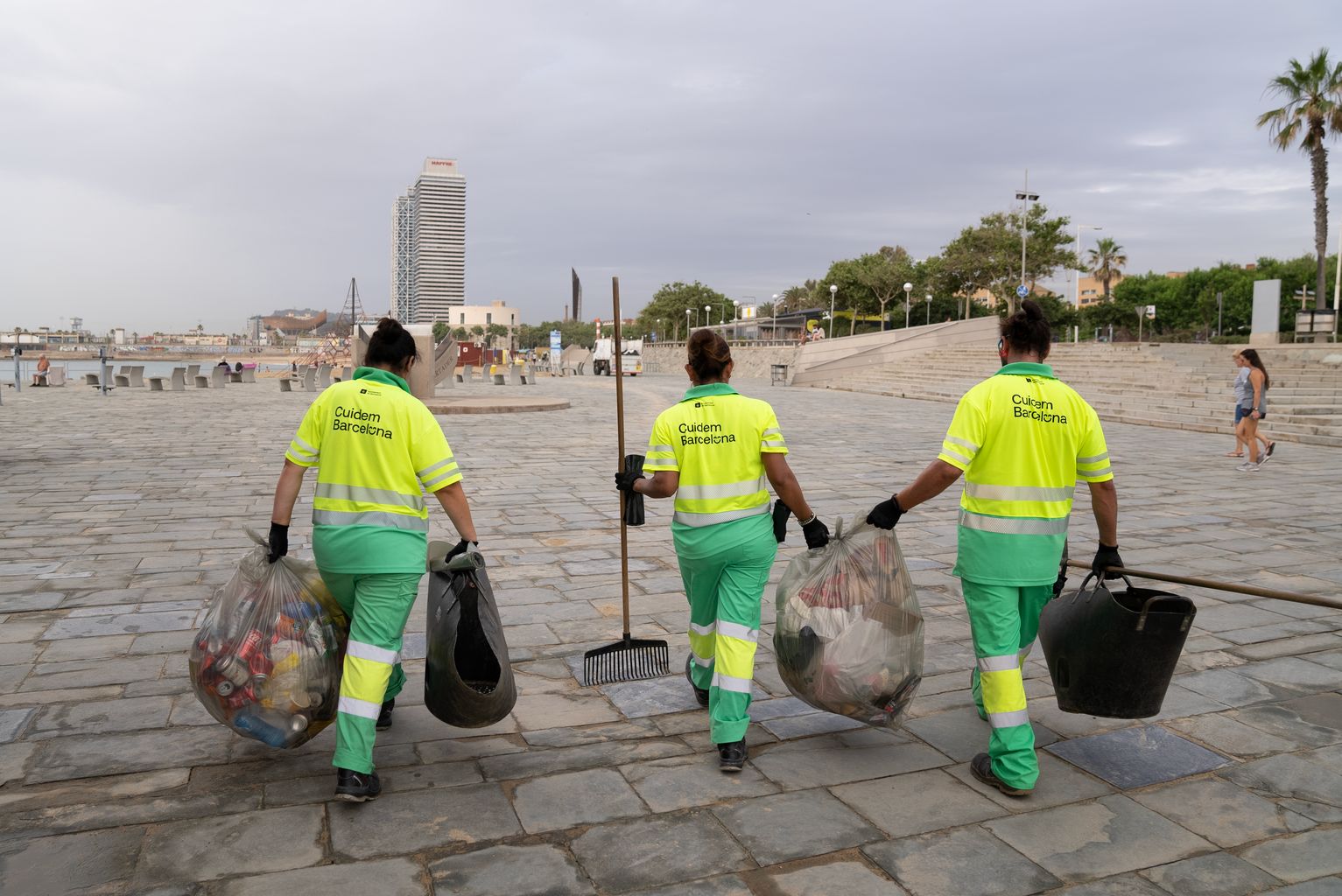 Personal del servicio de limpieza caminando por el paseo Marítim cargados con bolsas de residuos que han ido recogiendo durante las tareas de limpieza de playas