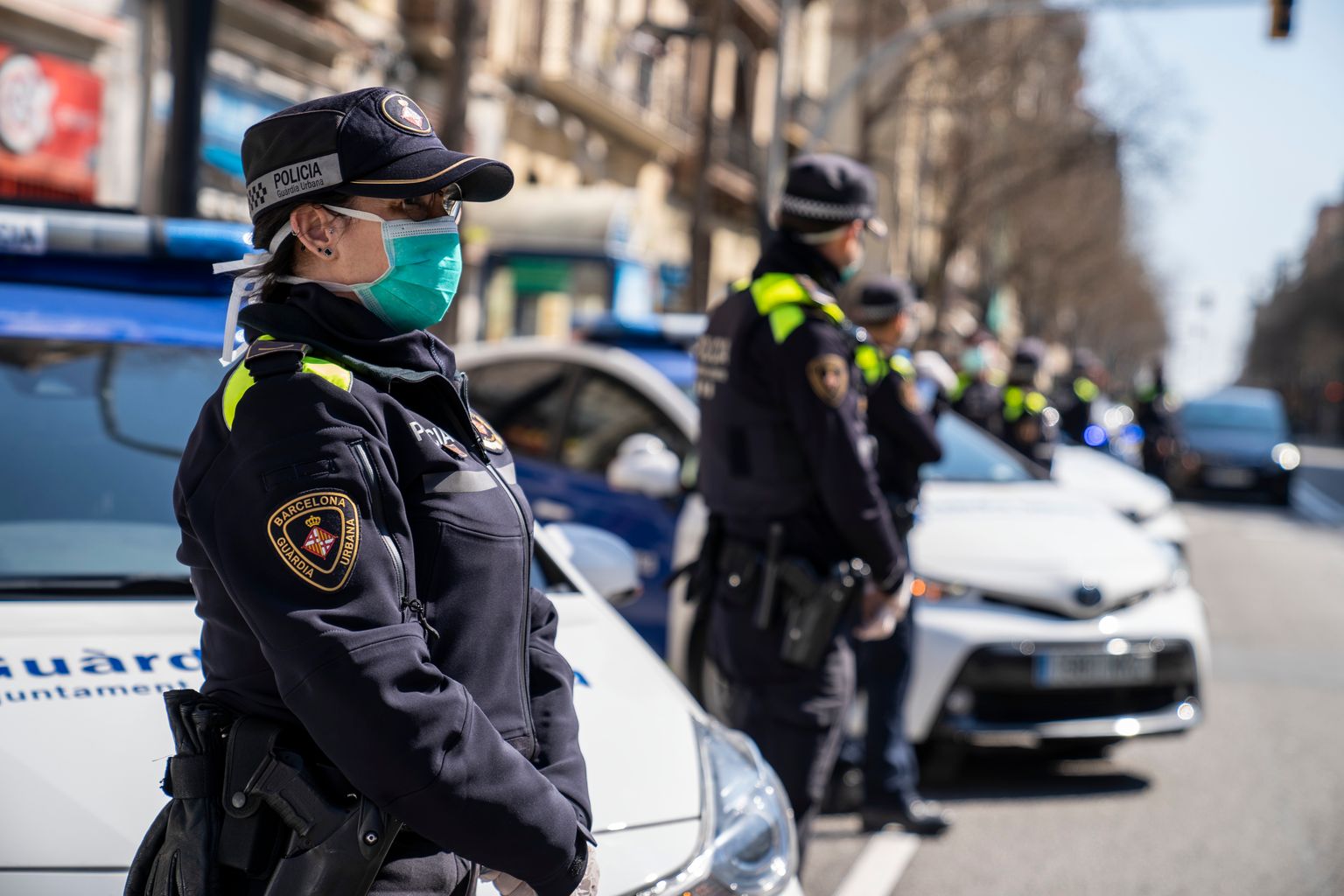 Cotxes i agents de la Guàrdia Urbana amb mascaretes i guants parats davant del Mercat d'Hostafrancs per retre l'homenatge als treballadors dels Mercats Municipals