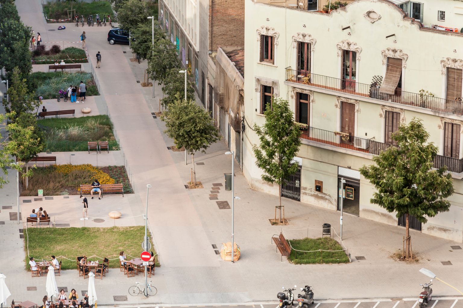 Superilla del Poblenou a l’altura del carrer de Roc Boronat, amb parterres i gent asseguda als bancs i les terrasses