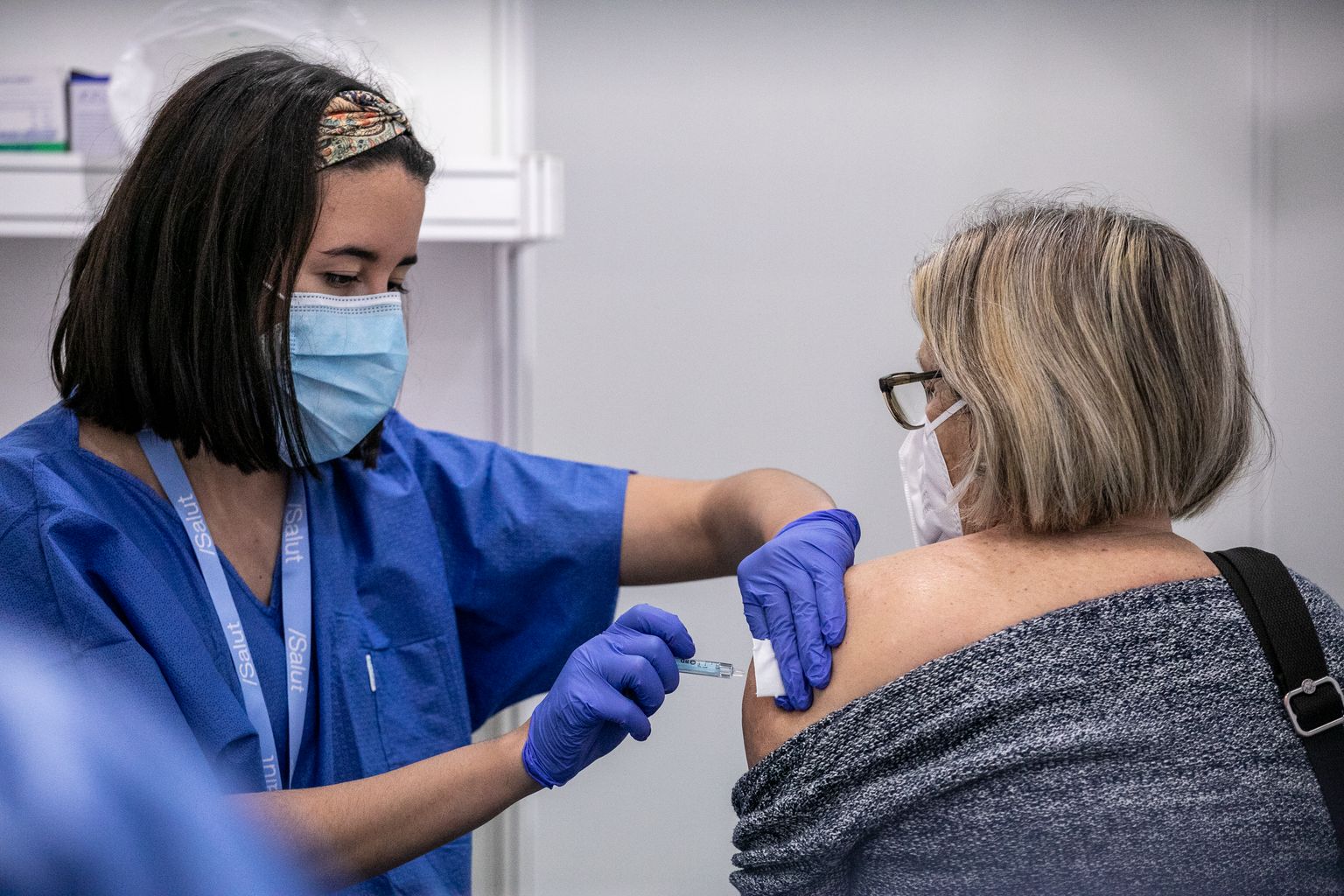 Una infermera administra una dosi de la vacuna a una dona que està asseguda a un dels box del punt de vacunació contra la covid-19
