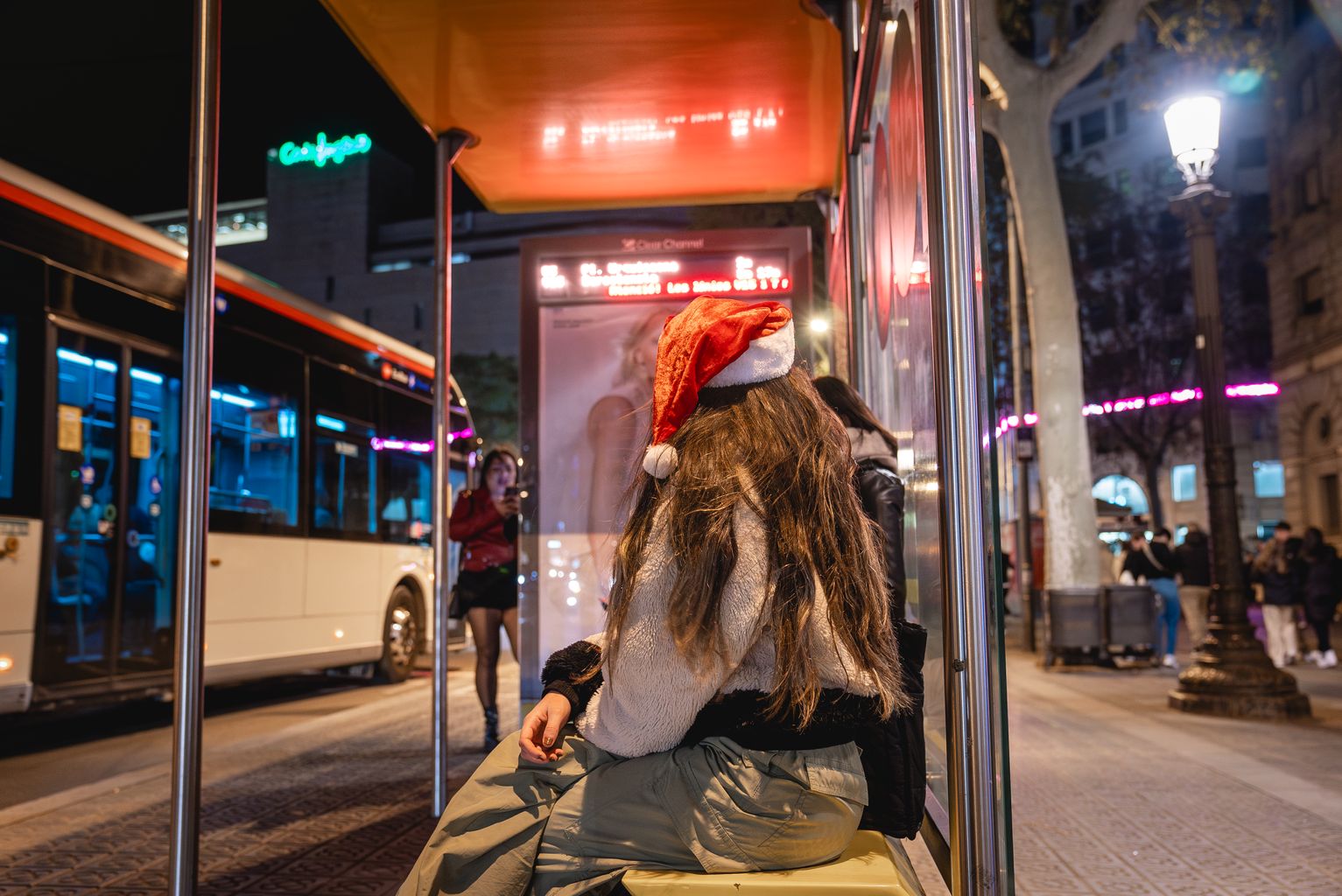 Jove amb un barret de Pare Noel espera l’autobús