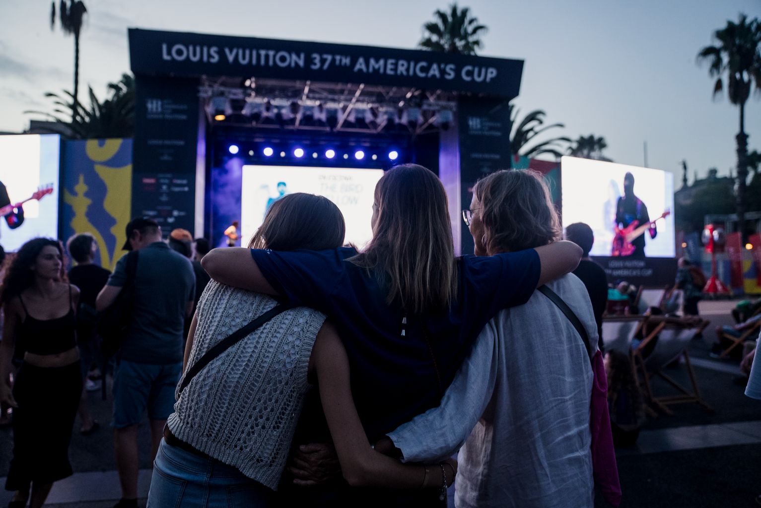 Un grup d’amics s’abracen mentre veuen el concert The Bird Yellow en el marc de la Regata Cultural de la Copa Amèrica