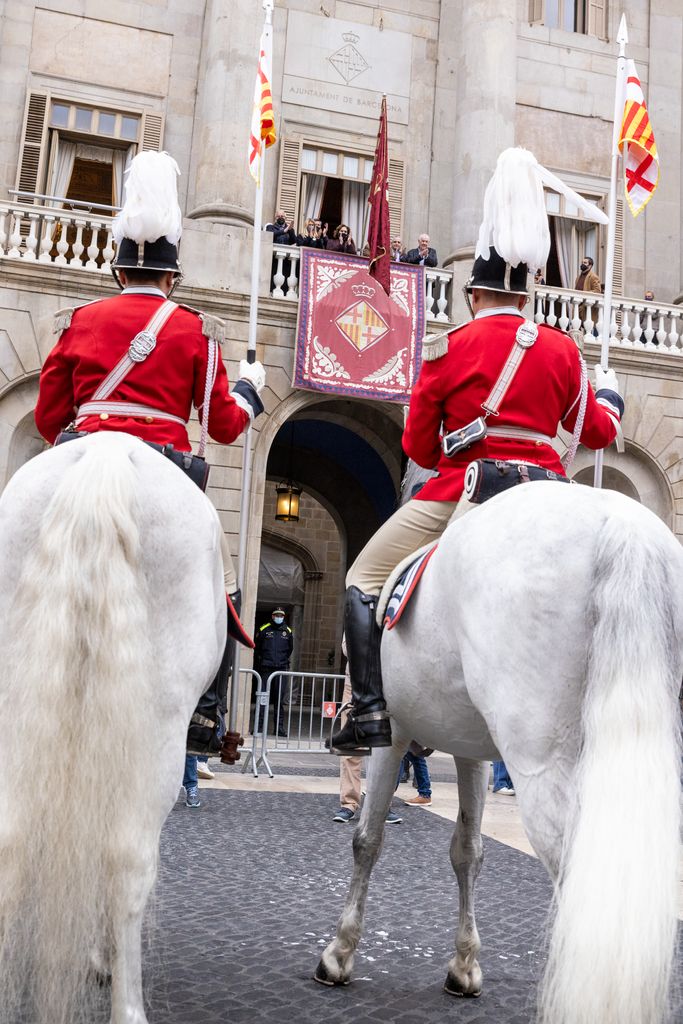 Ada Colau, amb el penó de Santa Eulàlia, al balcó de l'Ajuntament, acompanyada d'alguns regidors, mentre a la plaça presenta armes la Guàrdia Urbana a cavall i amb uniforme de gala.