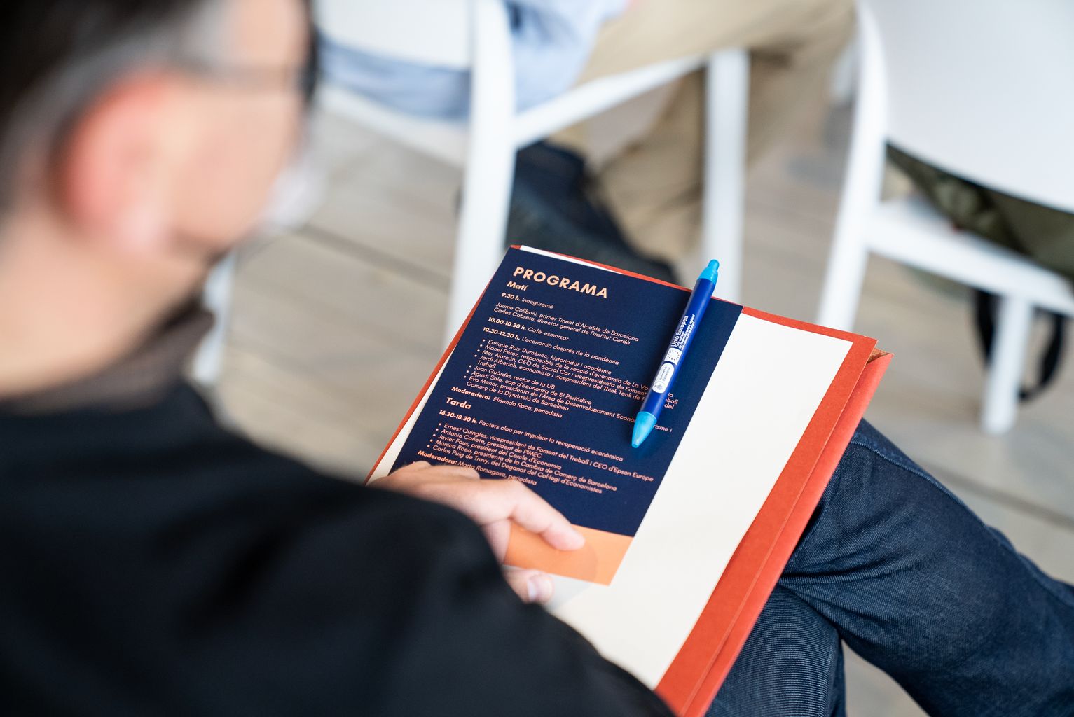 Un dels assistents al Primer Fòrum Nou Barris sosté una carpeta i el programa de l'acte sobre la falda