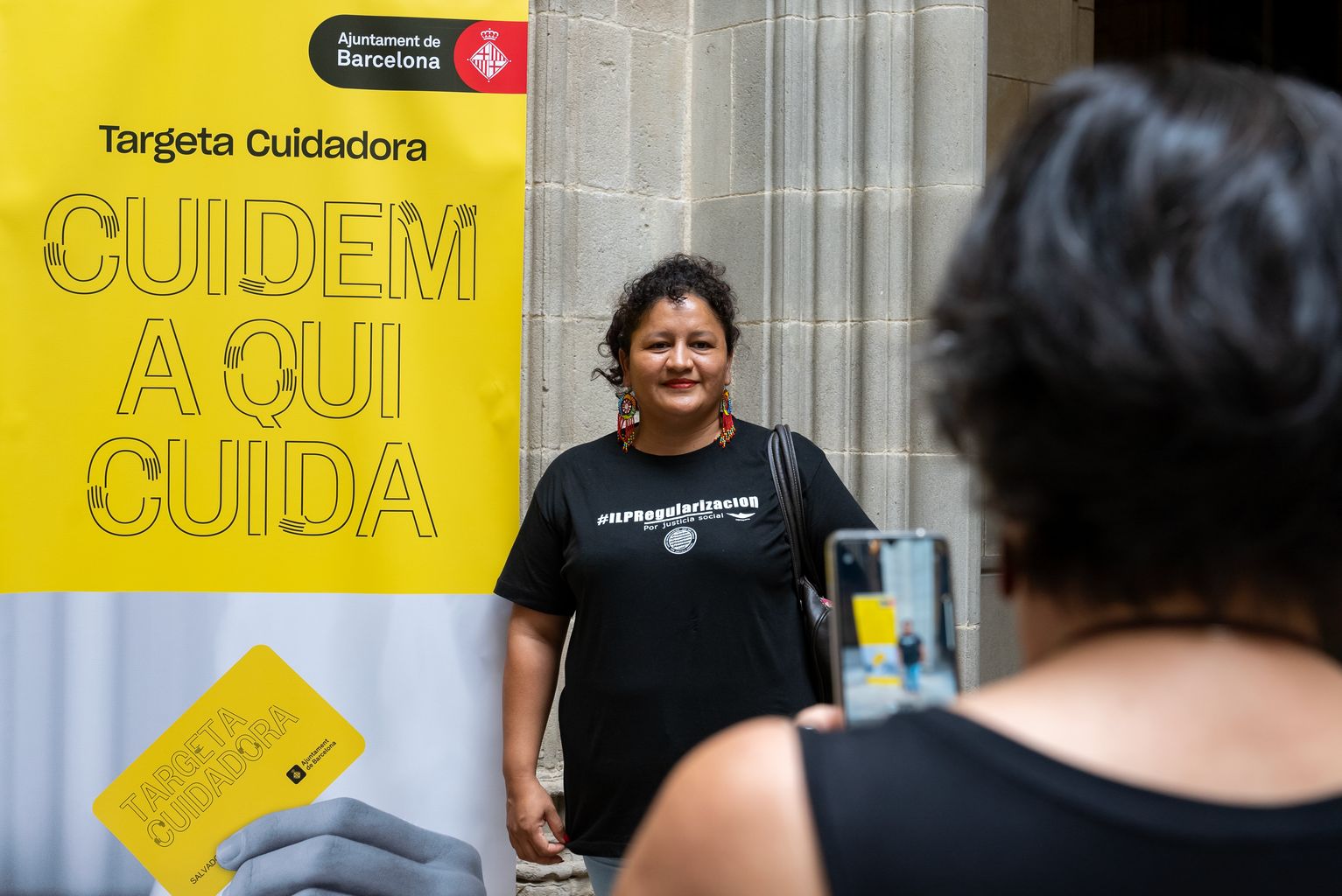 Una convidada al costat del cartell promocional de la nova Targeta Cuidadora de Barcelona.