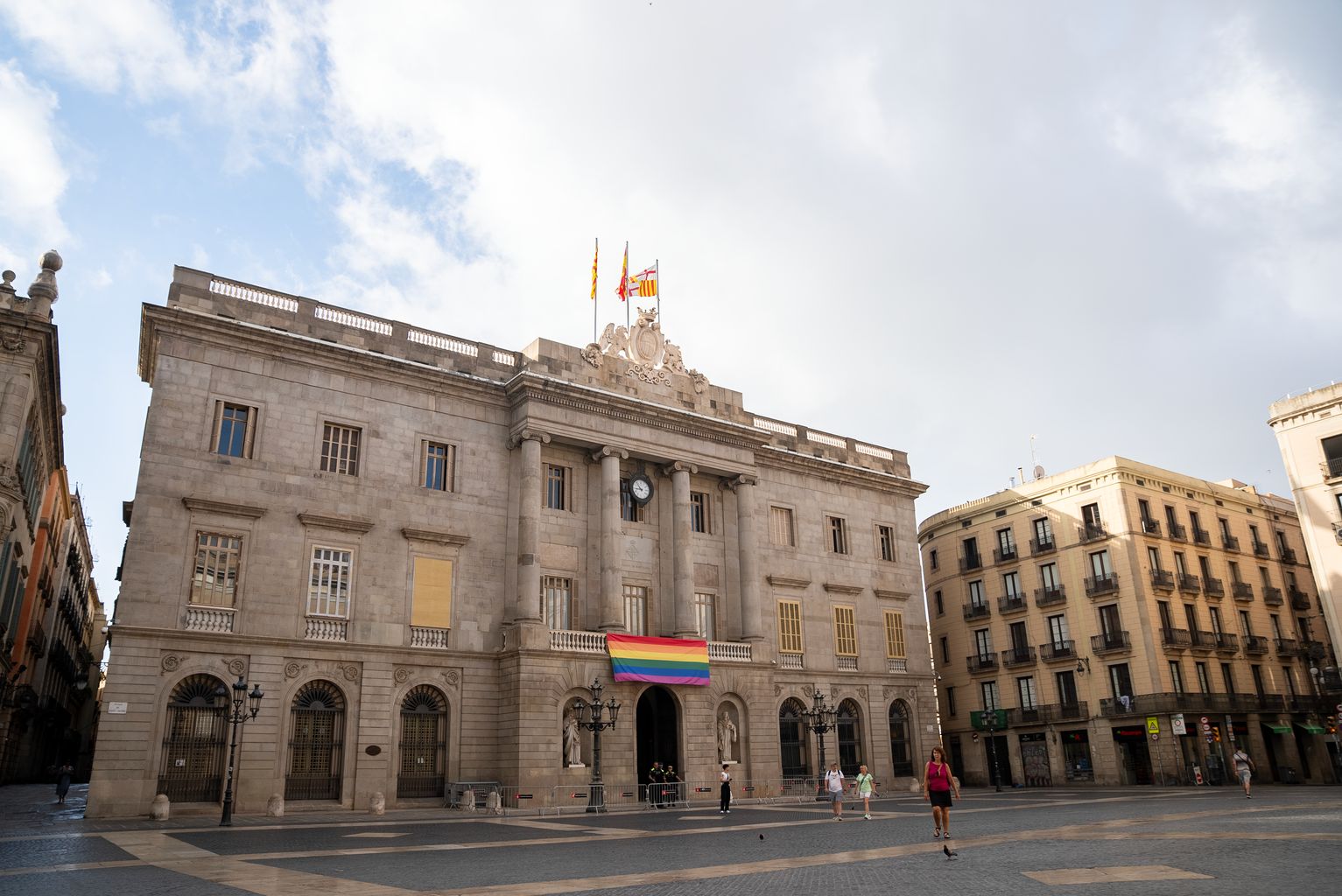Pla general de la plaça Sant Jaume i la façana de l'Ajuntament de Barcelona amb la bandera LGTBI penjada al balcó.