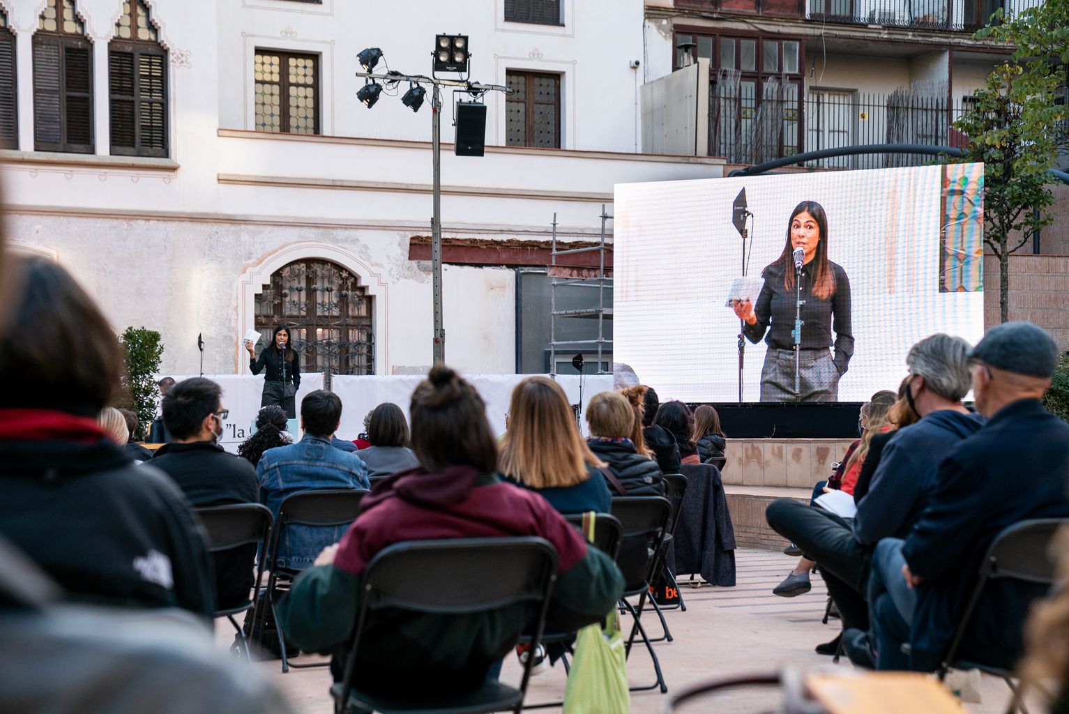 Una dona fa la presentació de l'activitat de la Biennal de pensament dalt de l'escenari dels jardins d'Agustí Centelles. Al seu costat, una gran pantalla per poder seguir l'acte