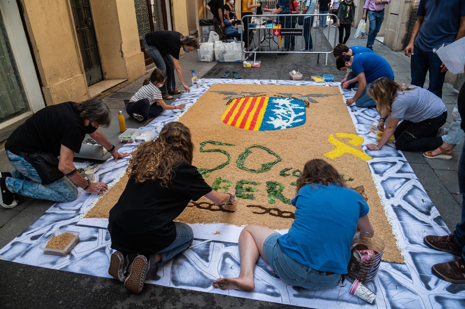 Miembros de la Comisión de Fiestas de la calle de la Llibertat elaboran la alfombra floral de la calle con ramillas, hojas verdes, arena, virutas de colores y flores