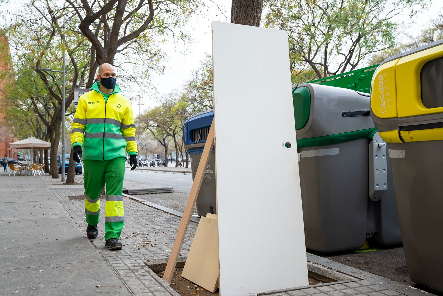 Un trabajador del servicio de limpieza (Cuidem Barcelona Residus) se dirige a recoger unos muebles que se encuentran en un alcorque delante de unos contenedores