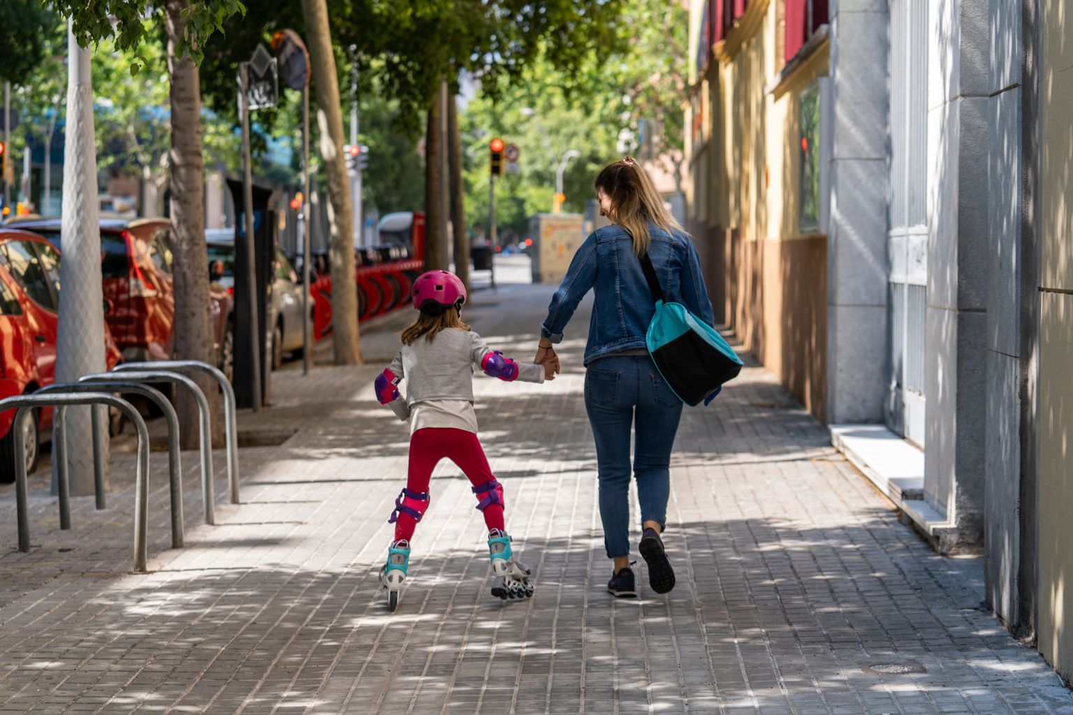 Una familia compuesta por una madre y su hija, con patines en línea, pasea de la mano por una acera ancha